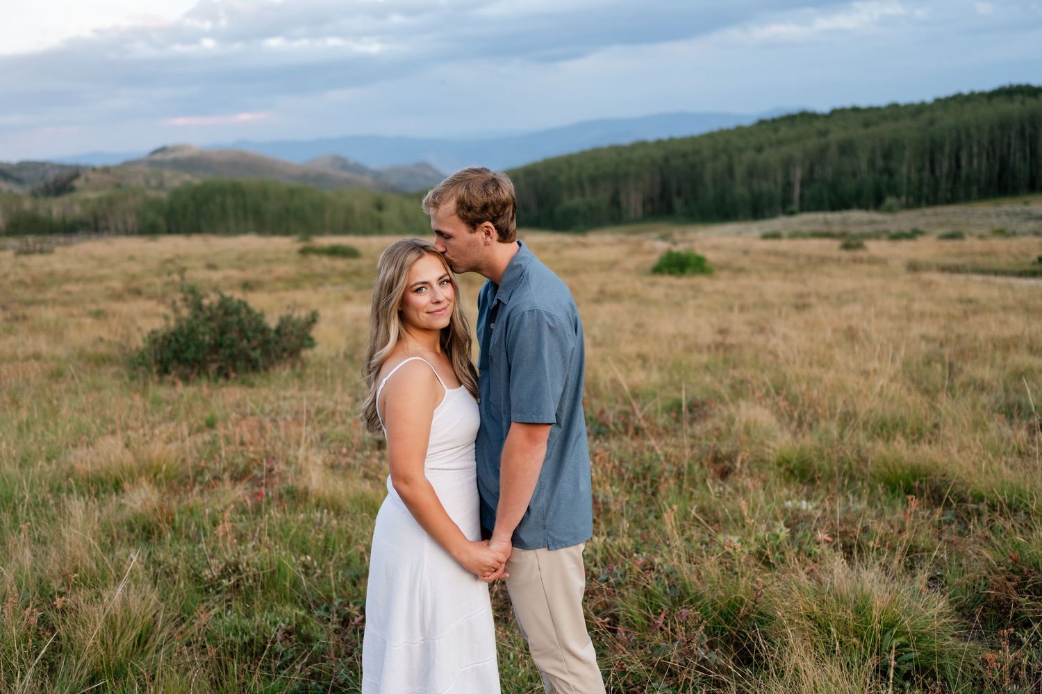 Park City mountain engagement photography at sunset. Man kissing girl on her forehead on the mountain top.