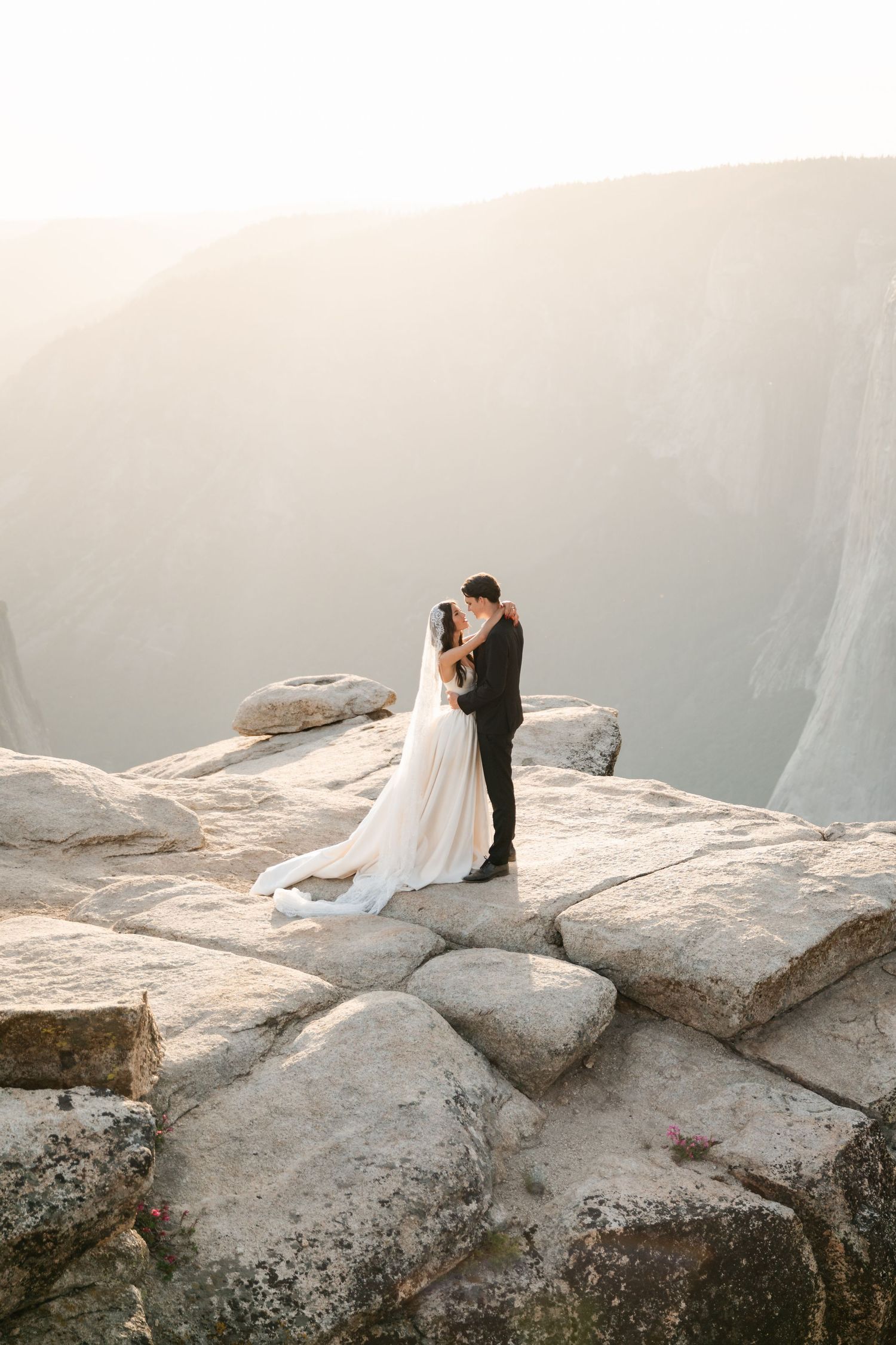 Bride and groom embracing on granite rocks at Taft Point in Yosemite at sunset.