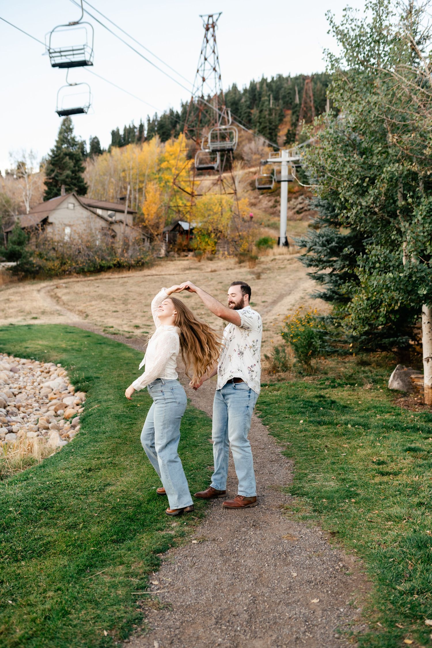 Playful couple enjoying a fall day near ski lifts and mountain trails with autumn foliage in the background. Engagement Photographer.