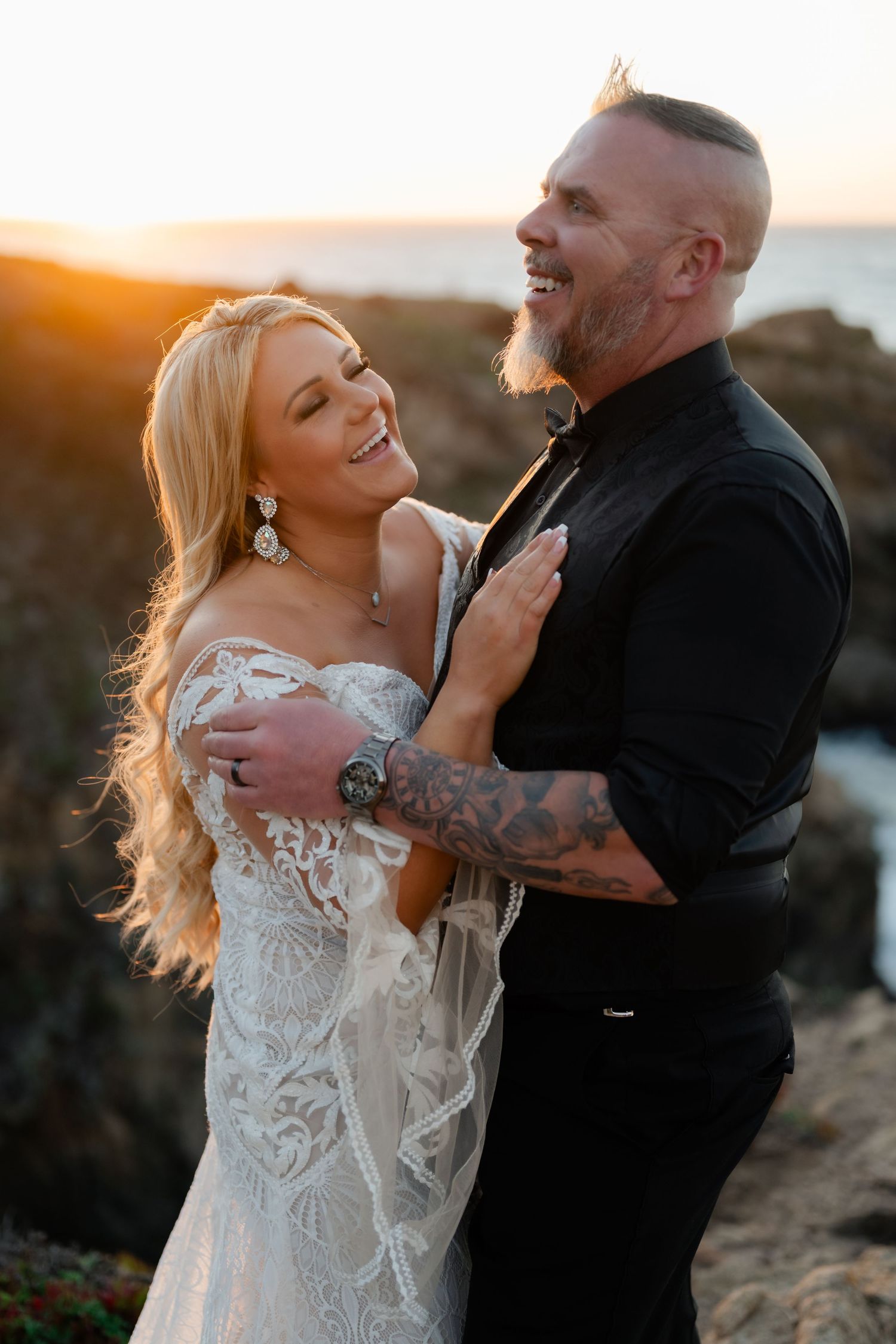 Joyful wedding couple shares intimate moment on coastal cliffs at sunset.