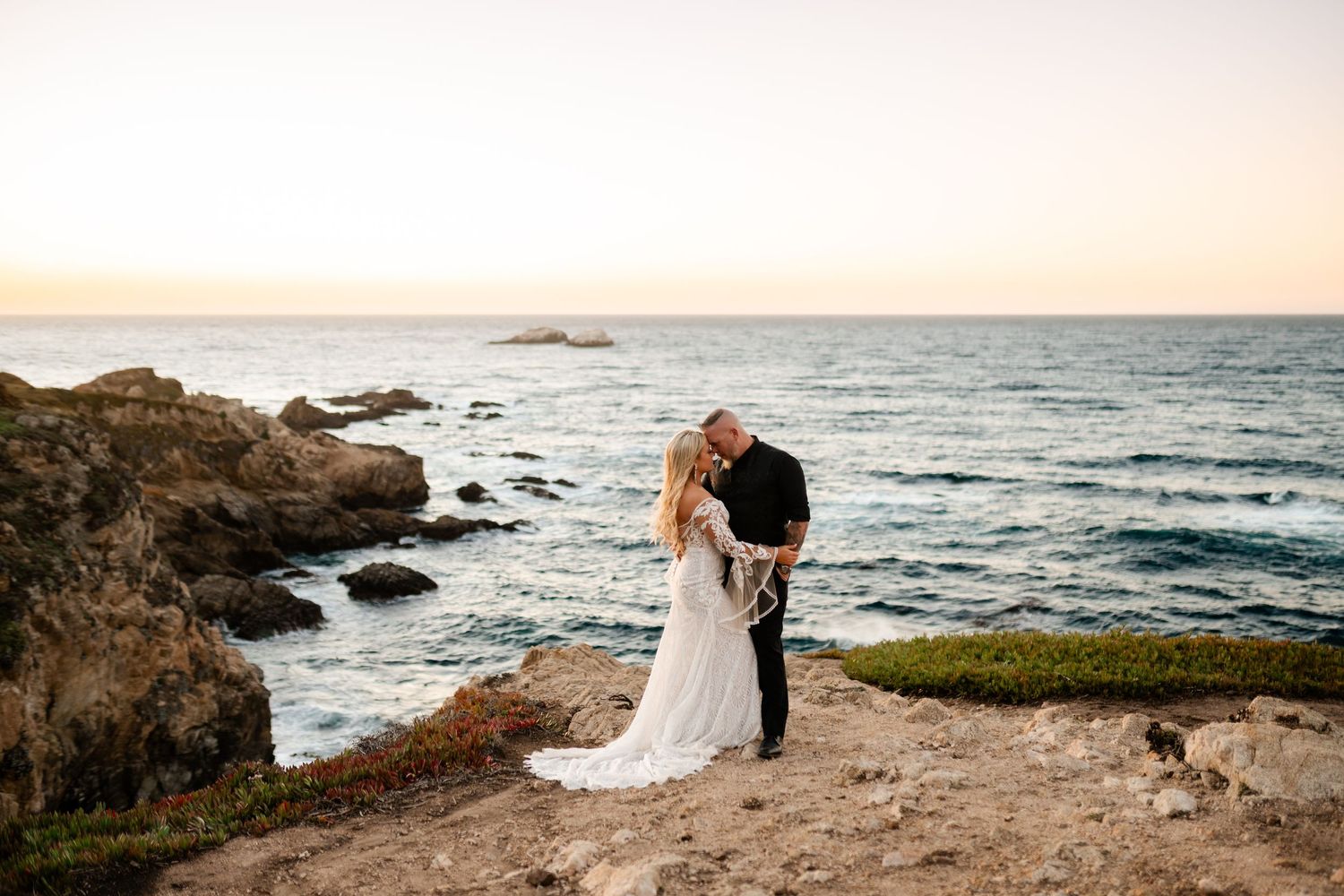 A dramatic wedding portrait on rugged California coastline during golden hour.