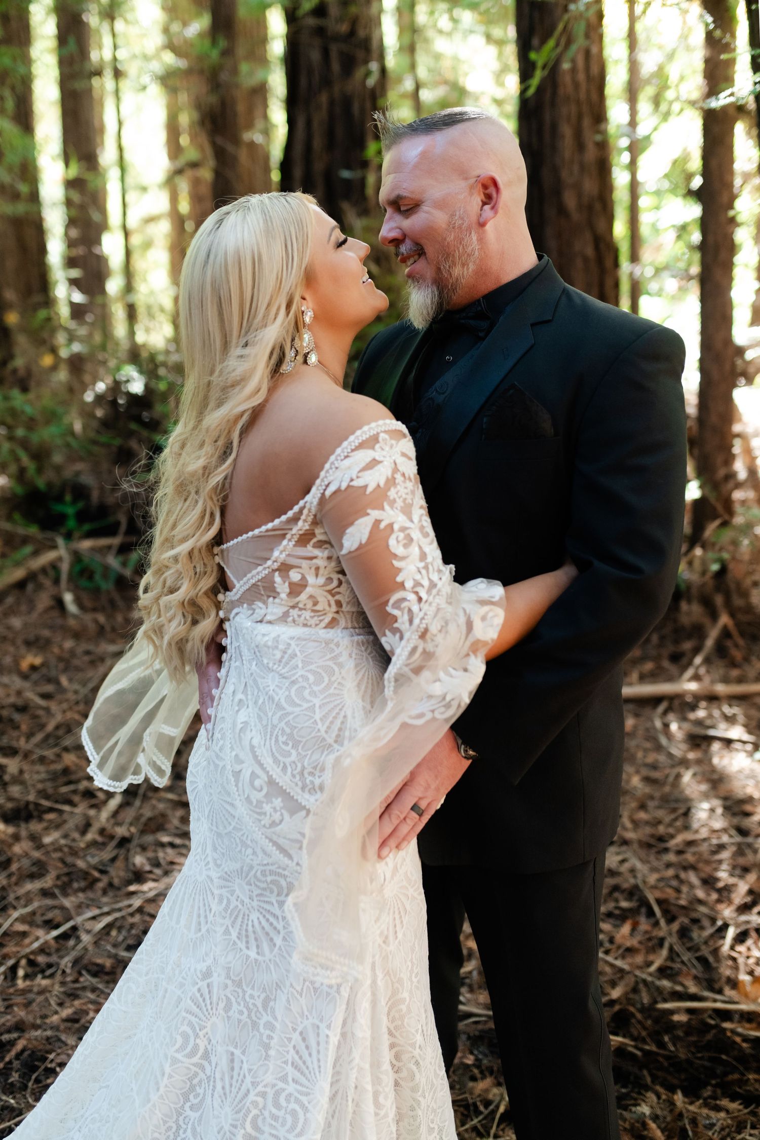 Couple sharing intimate moments in a sunlit forest wearing wedding attire.