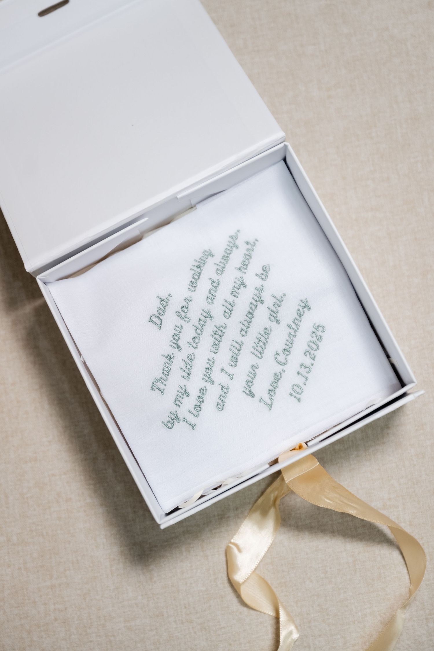 Wedding invitation box with elegant calligraphy text and gold ribbon detail on a neutral background.