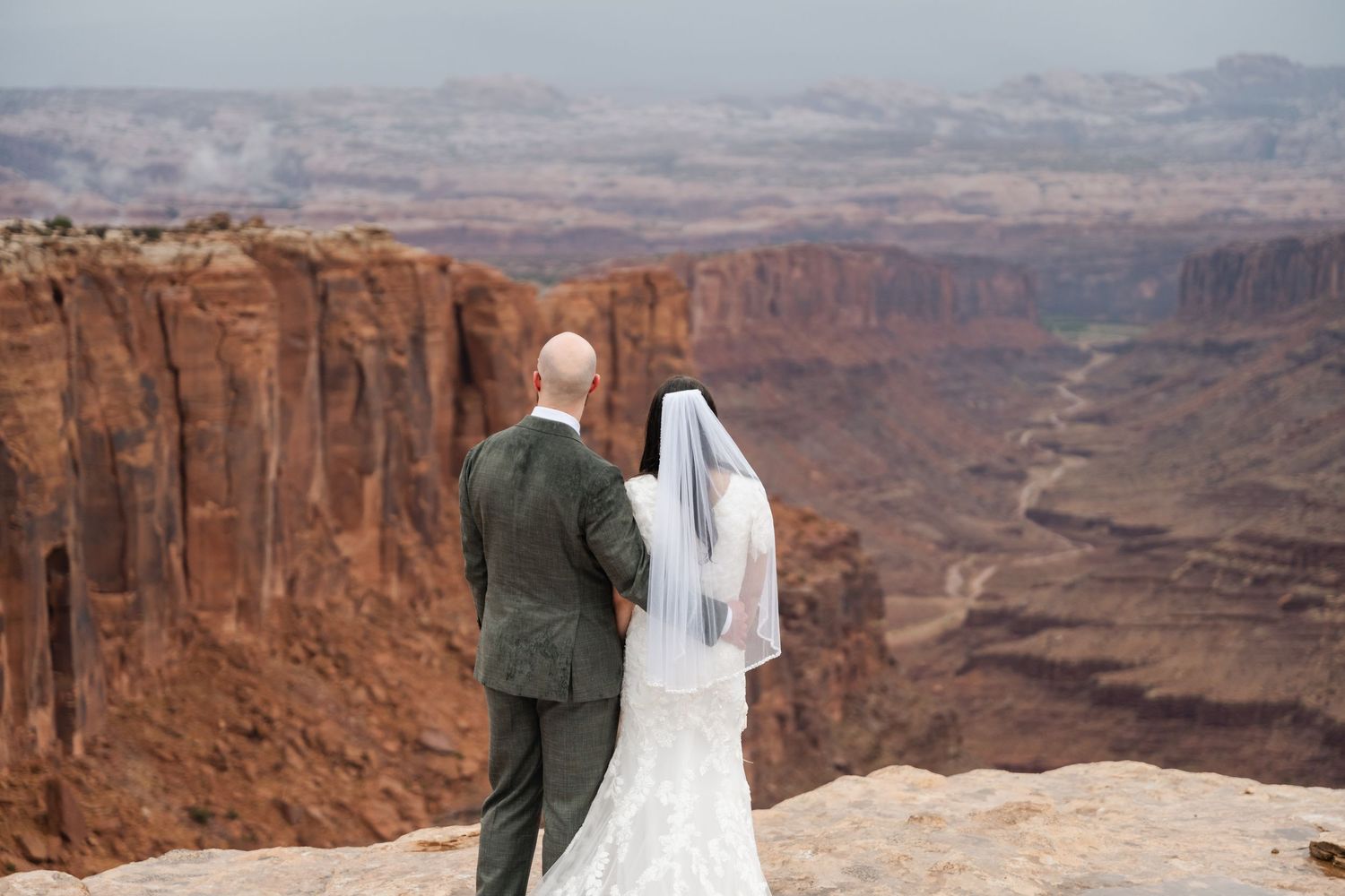 A wedding ceremony silhouetted against a vast desert canyon landscape.