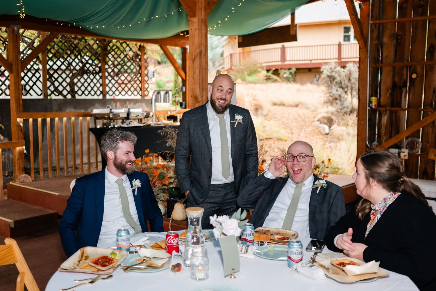 Wedding guests enjoying dinner at tables under a covered outdoor pavilion.