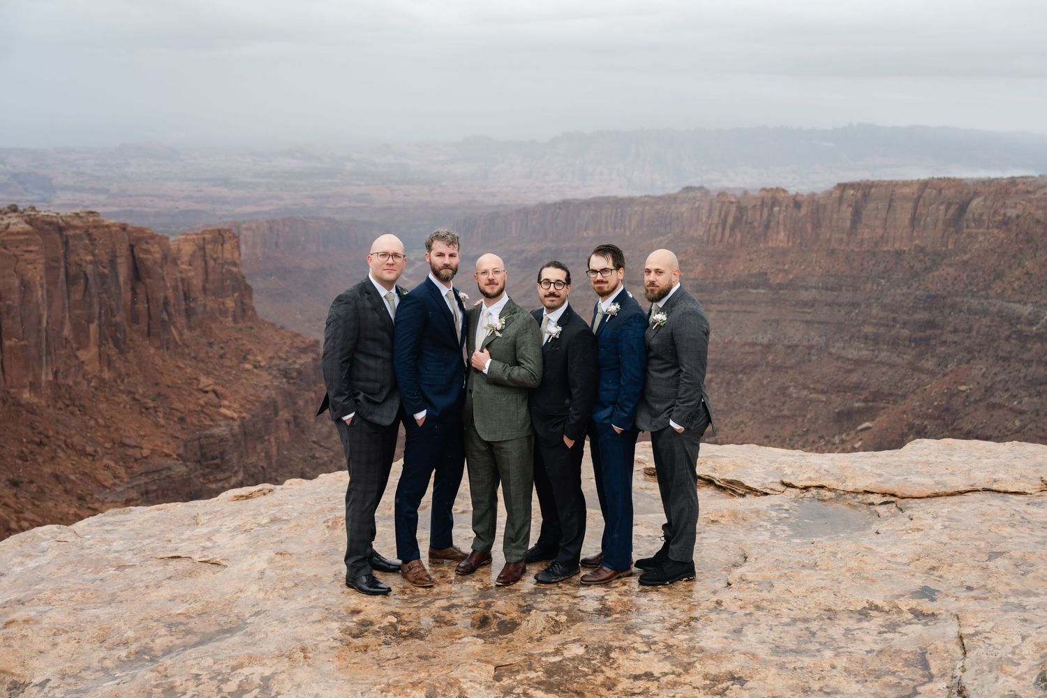 Wedding party members lined up for photos on a scenic desert canyon overlook.