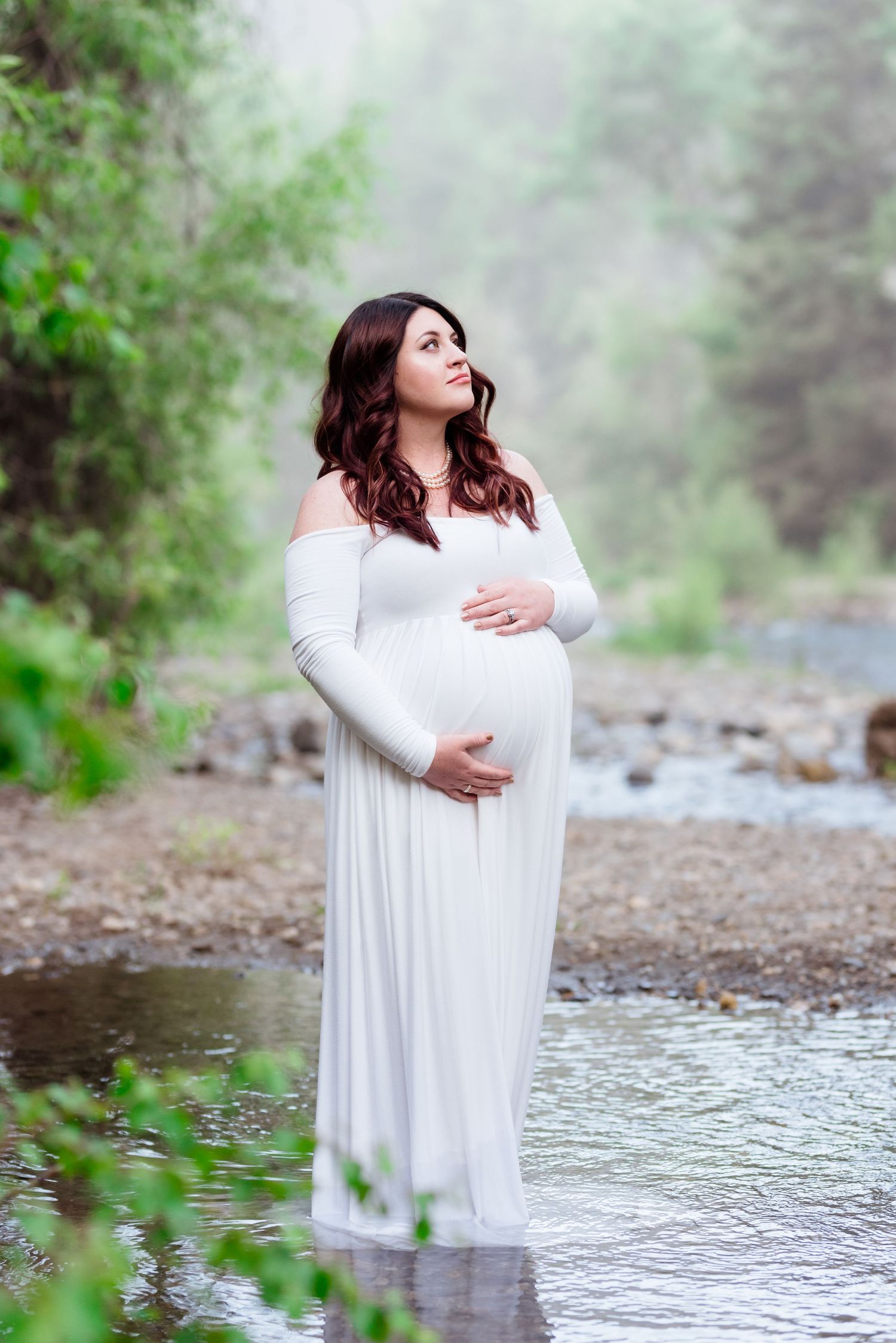 A figure in a flowing white dress stands near a misty lake's edge in a serene forest setting.