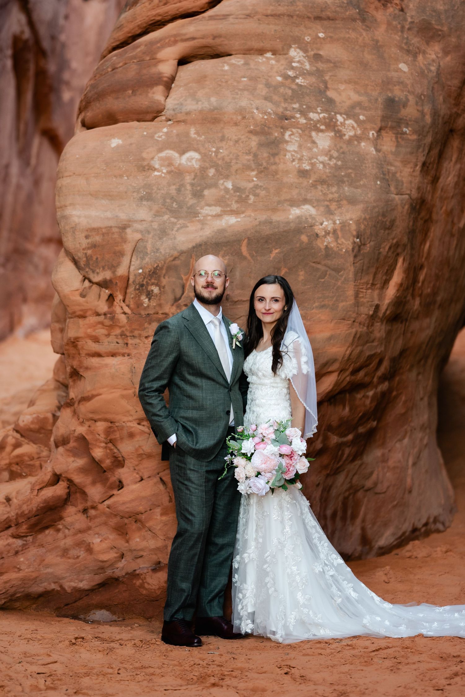 Wedding couple poses against red rock canyon walls in romantic desert elopement ceremony.