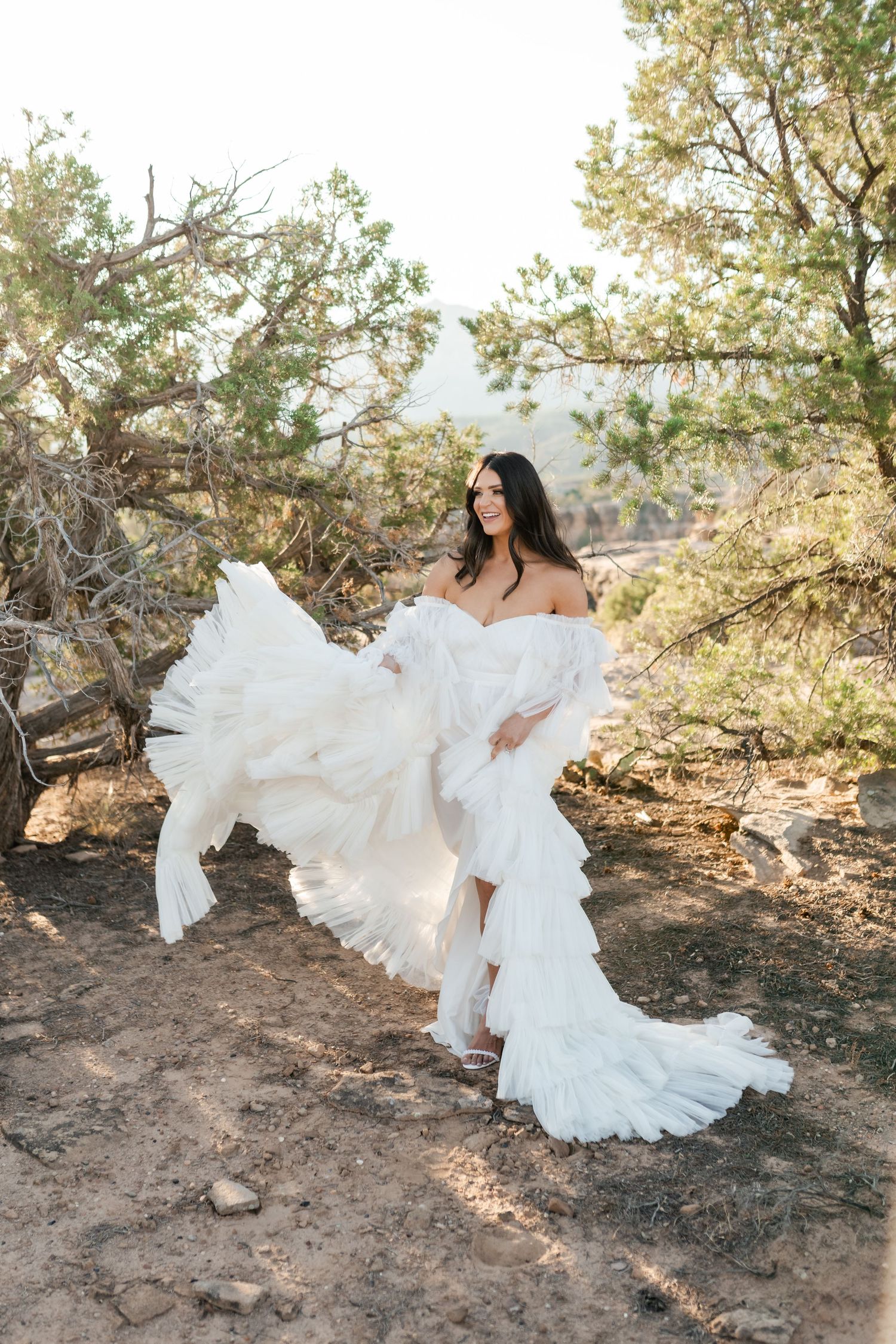 Zion destination photographer, White wedding dress flows dramatically in desert breeze against sunlit trees and rocks.