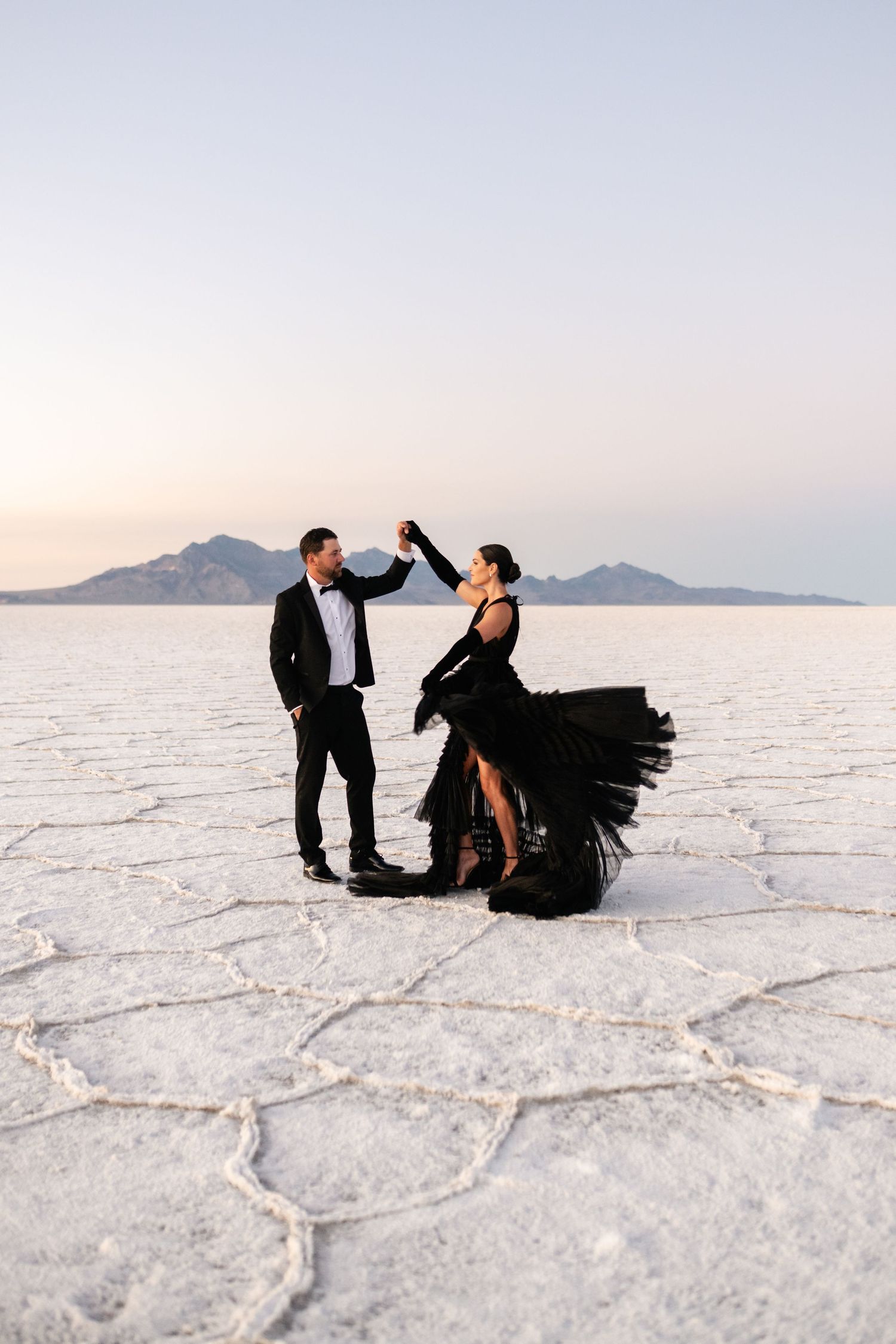 Utah Salt Flats Photographer. A couple dancing on the Bonneville Salt Flats at sunset with mountains in the background.