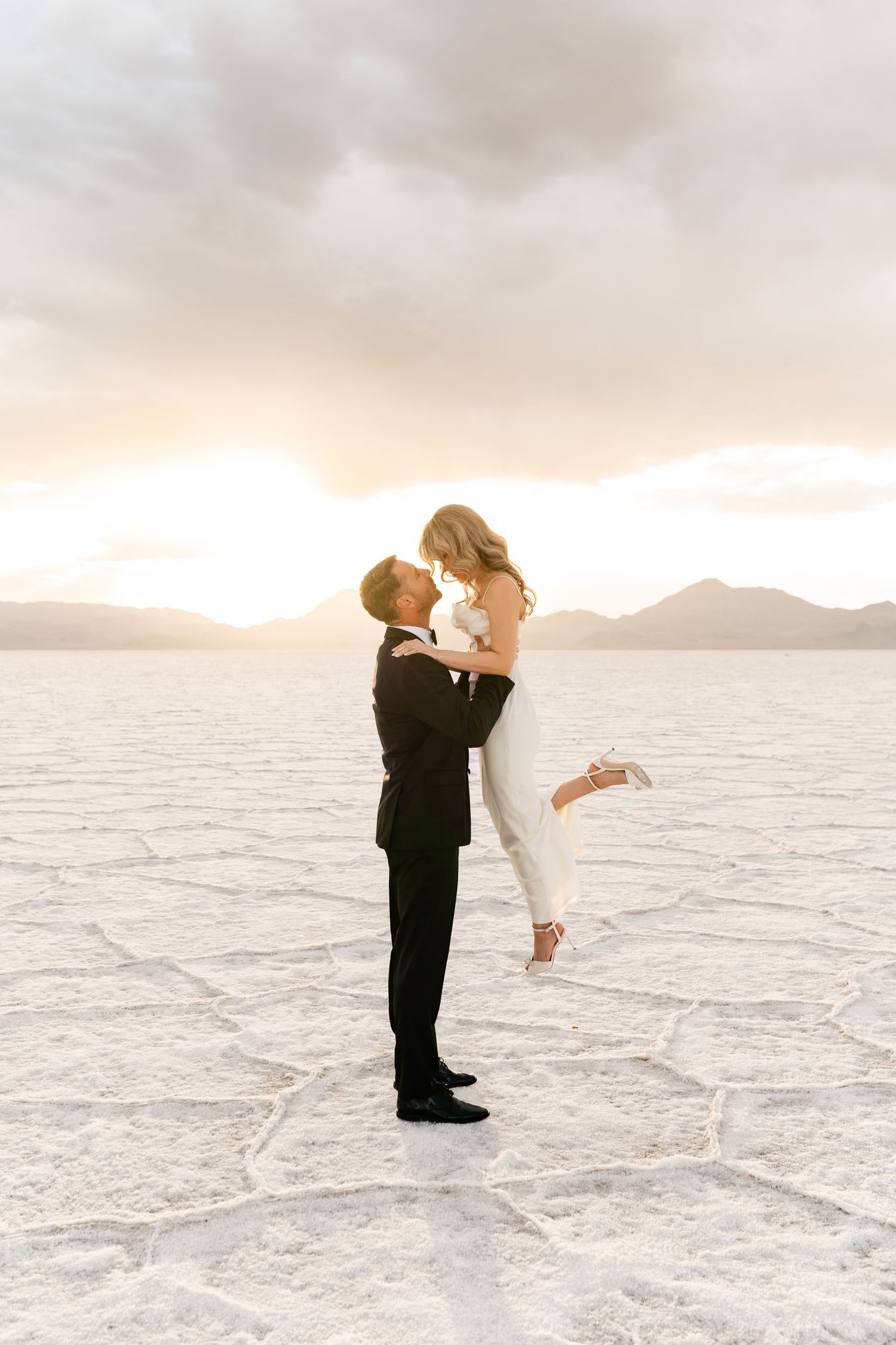 Salt Flats Elopement Photographer. Newlyweds share an intimate moment on salt flats during golden hour with mountains behind them.