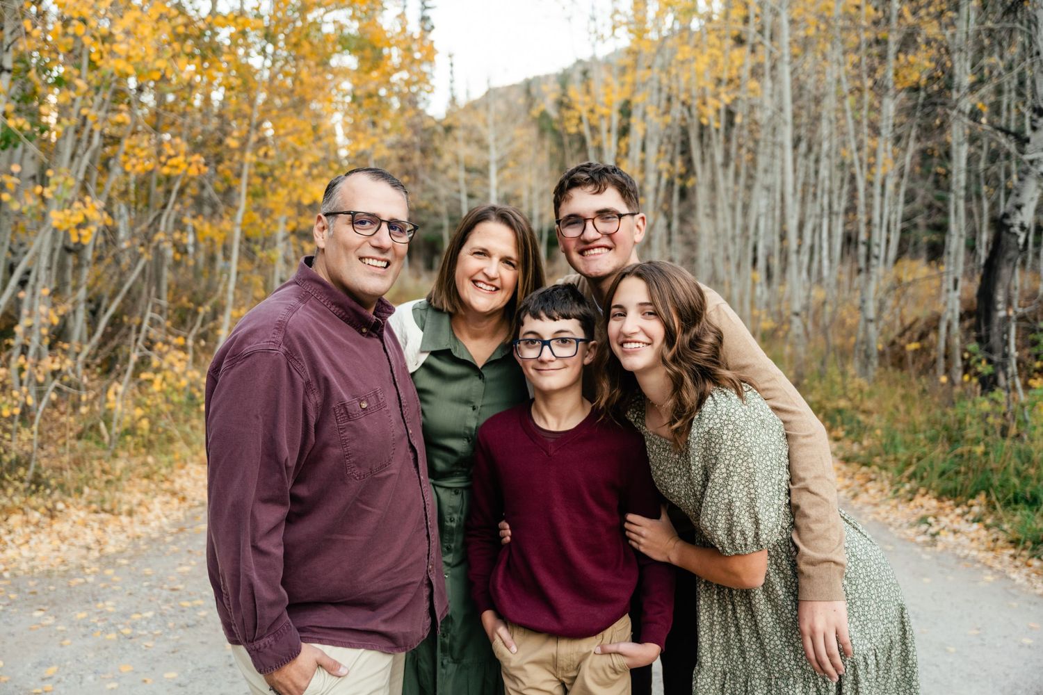 A group poses together outdoors surrounded by golden autumn aspen trees on a forest path.