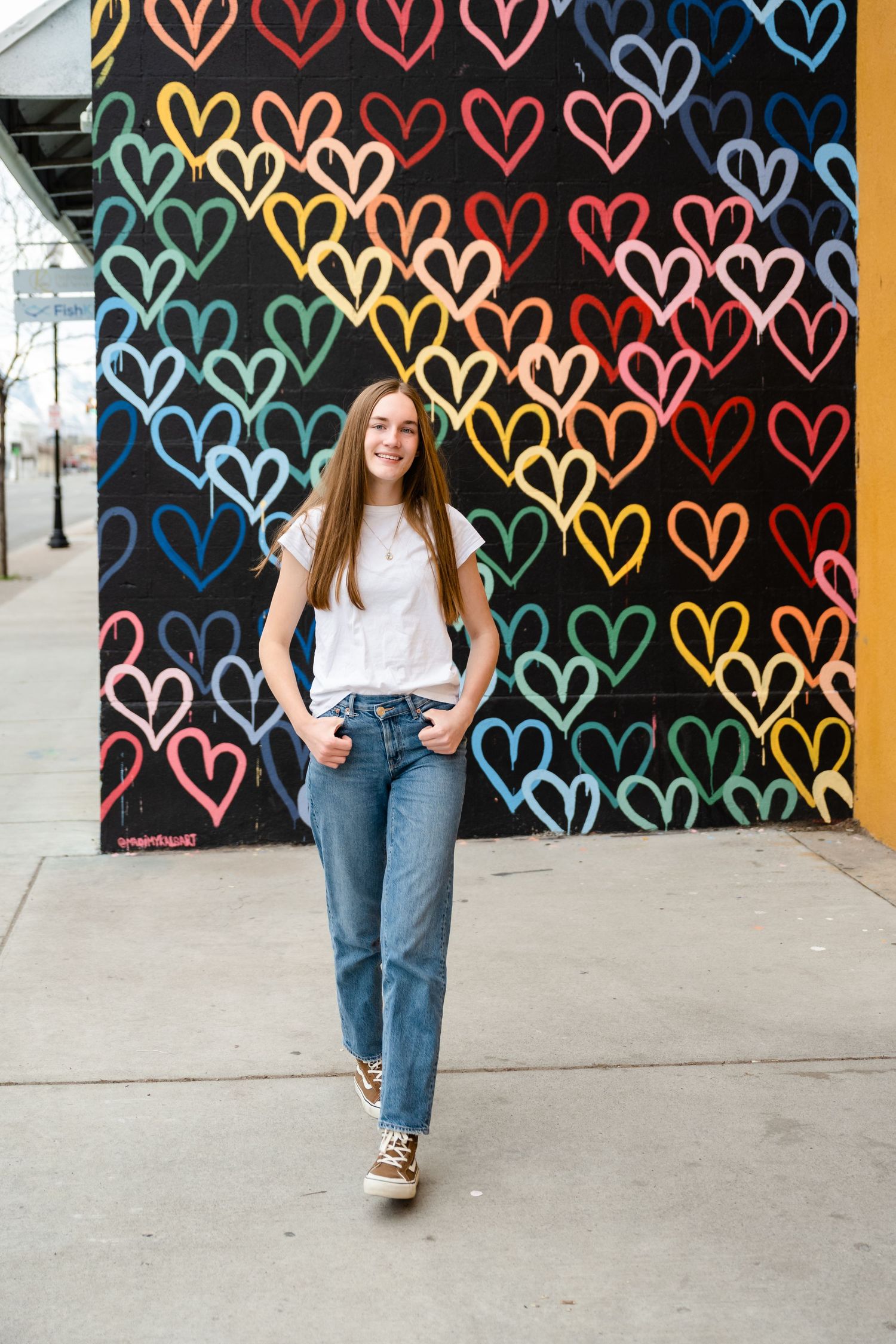 A person poses against a vibrant mural wall decorated with colorful heart patterns in a series of casual fashion photos.