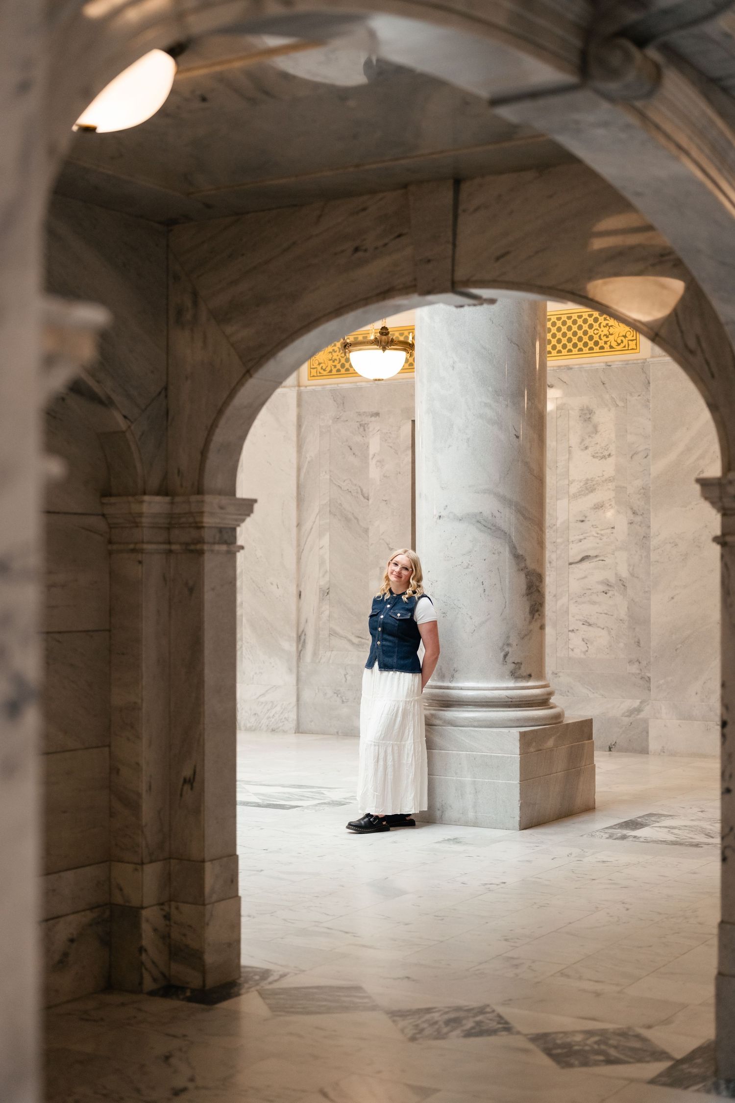 A couple embraces in a romantic moment under stone archways in a historic building's white marble corridor.