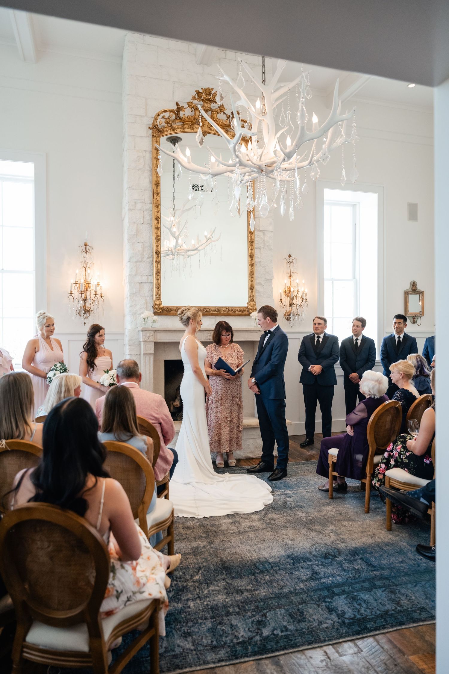 Elegant indoor wedding ceremony with antler chandelier, gold mirror, and guests seated in wooden chairs in Park City.