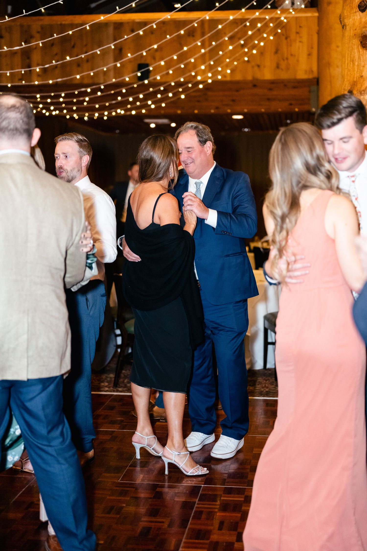 Wedding guests dancing and celebrating on a wooden dance floor under twinkling lights.