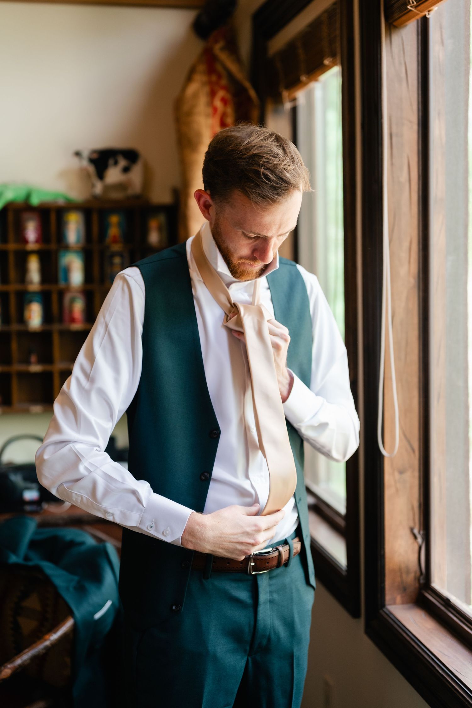 Person in formal attire adjusting clothing by window in preparation for event.