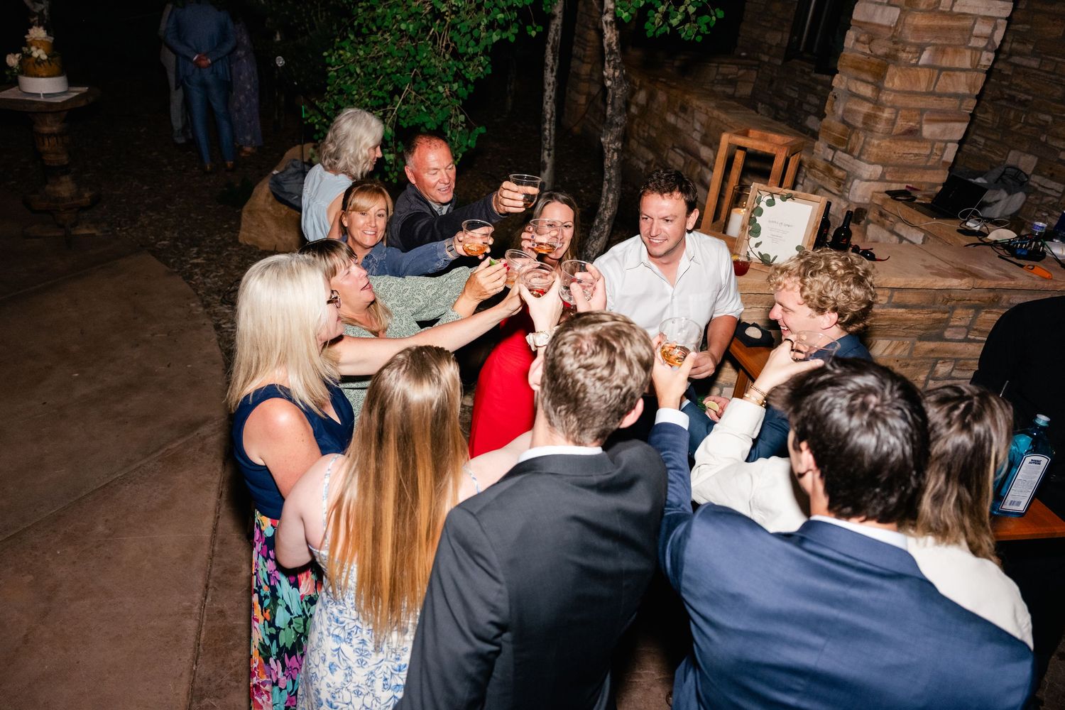 Wedding guests gathered in a circle sharing drinks and celebrating at an evening reception.