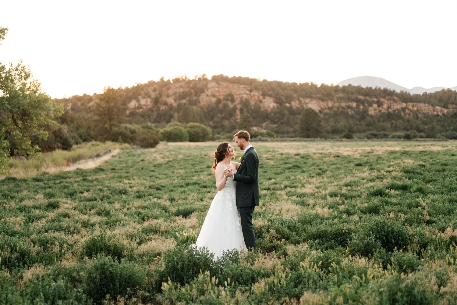 Couple embraces in a scenic mountain meadow during golden hour sunset.