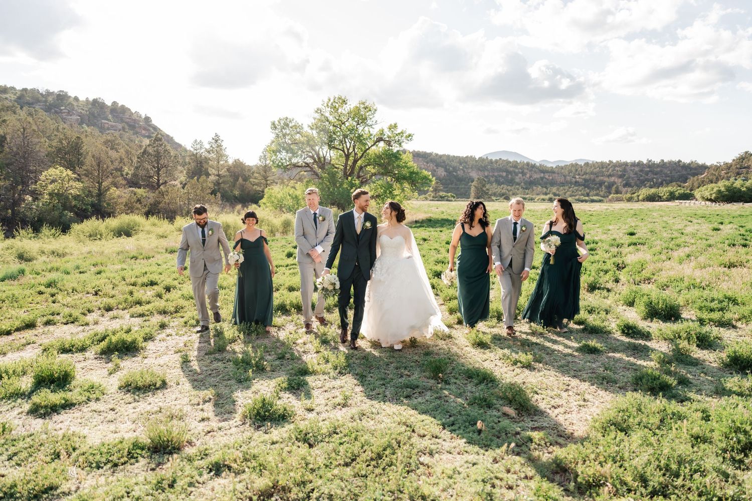 A group of people stand together in a scenic outdoor field with mountains and natural landscape in the background.