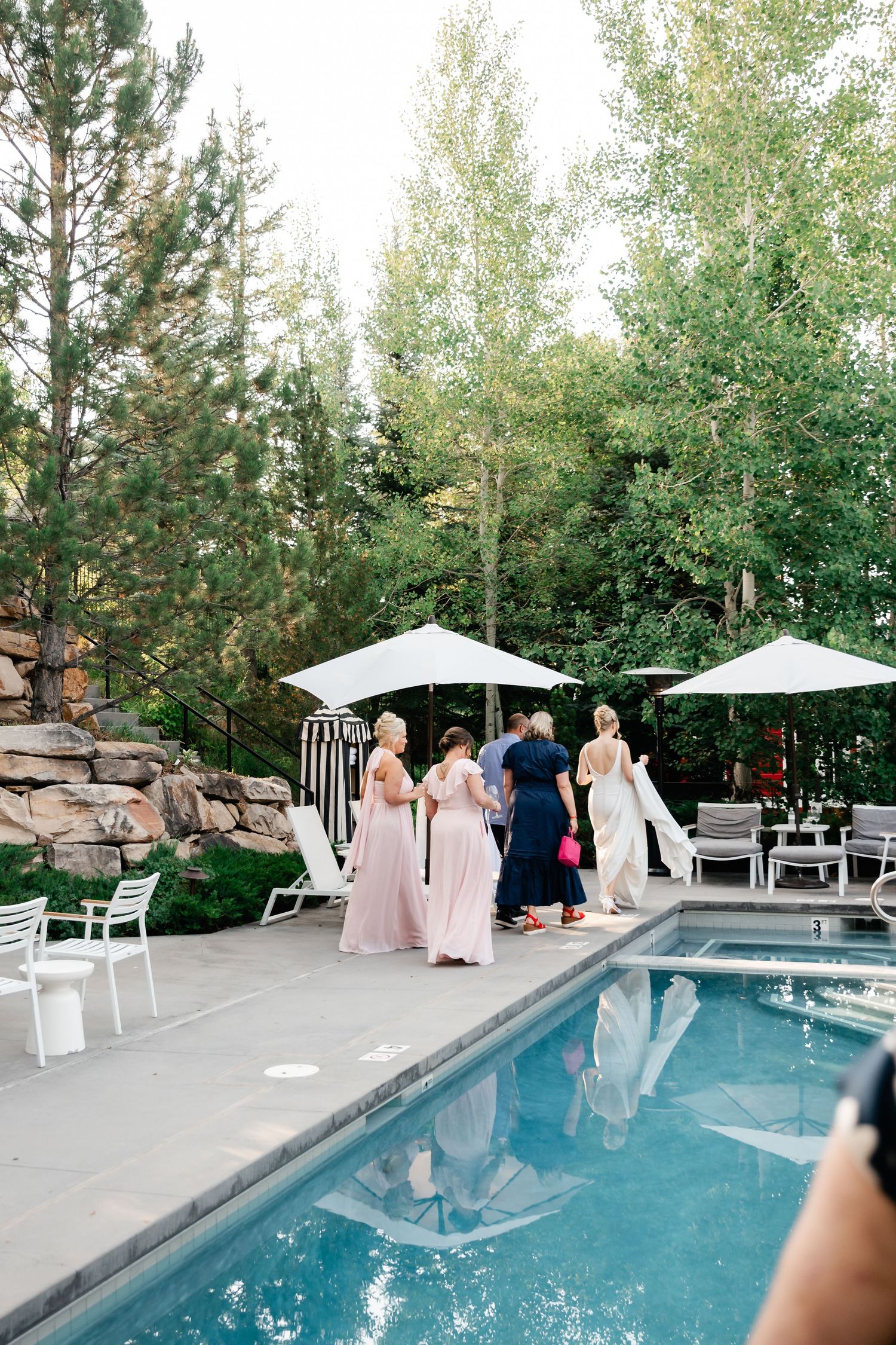 Poolside wedding reception with guests gathered around a modern swimming pool and white umbrellas.