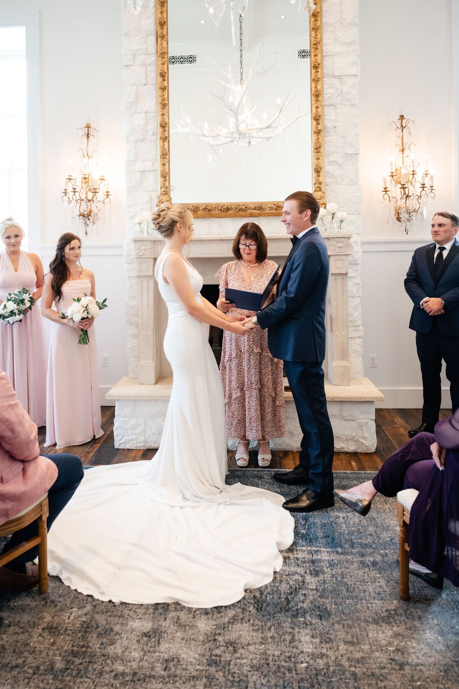 Wedding ceremony moments unfold in an elegant white room with ornate gold mirrors and chandeliers.