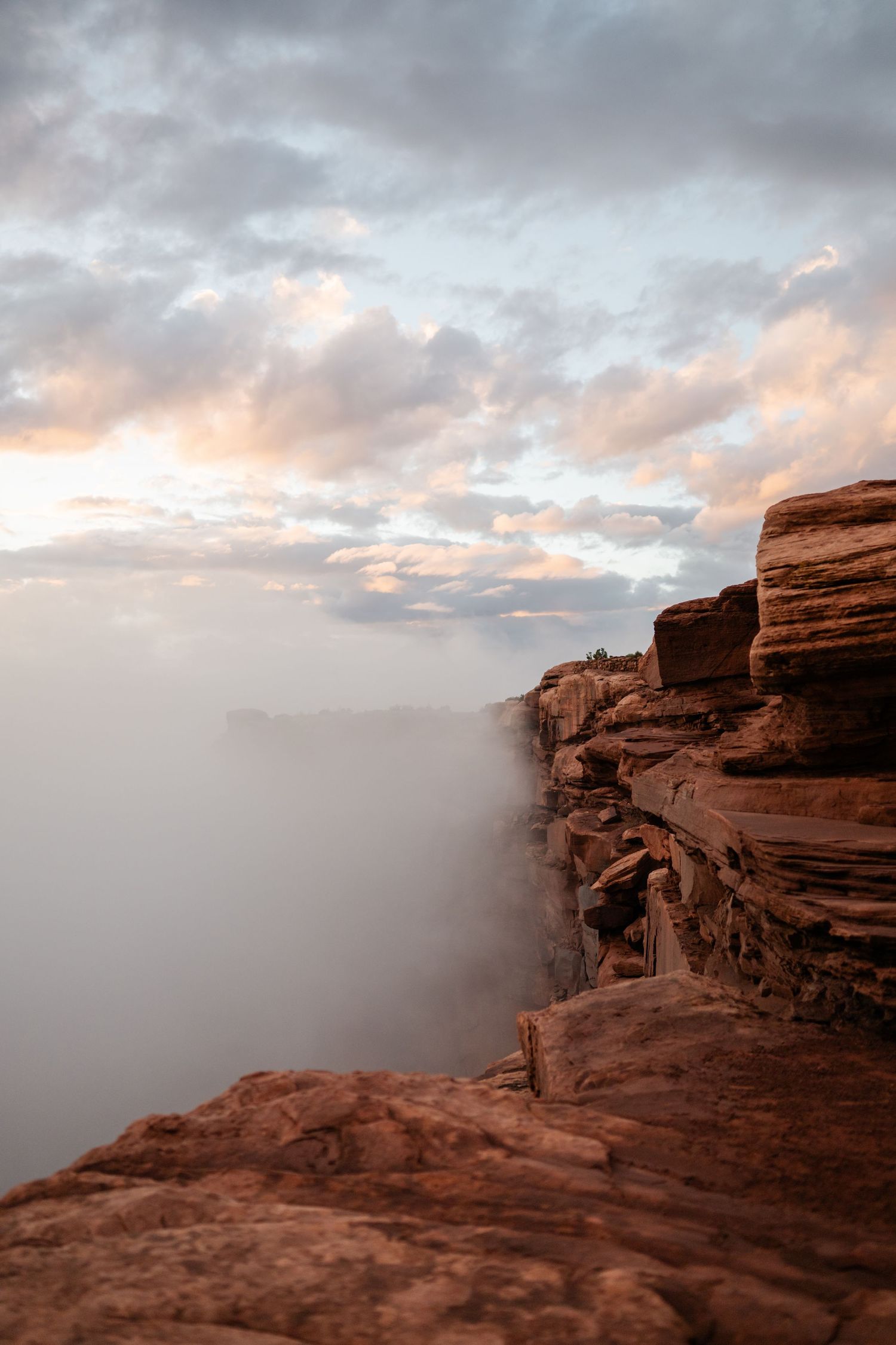 Dramatic cloudy sunset over red rock cliffs in a desert landscape with fog rolling through the canyon.