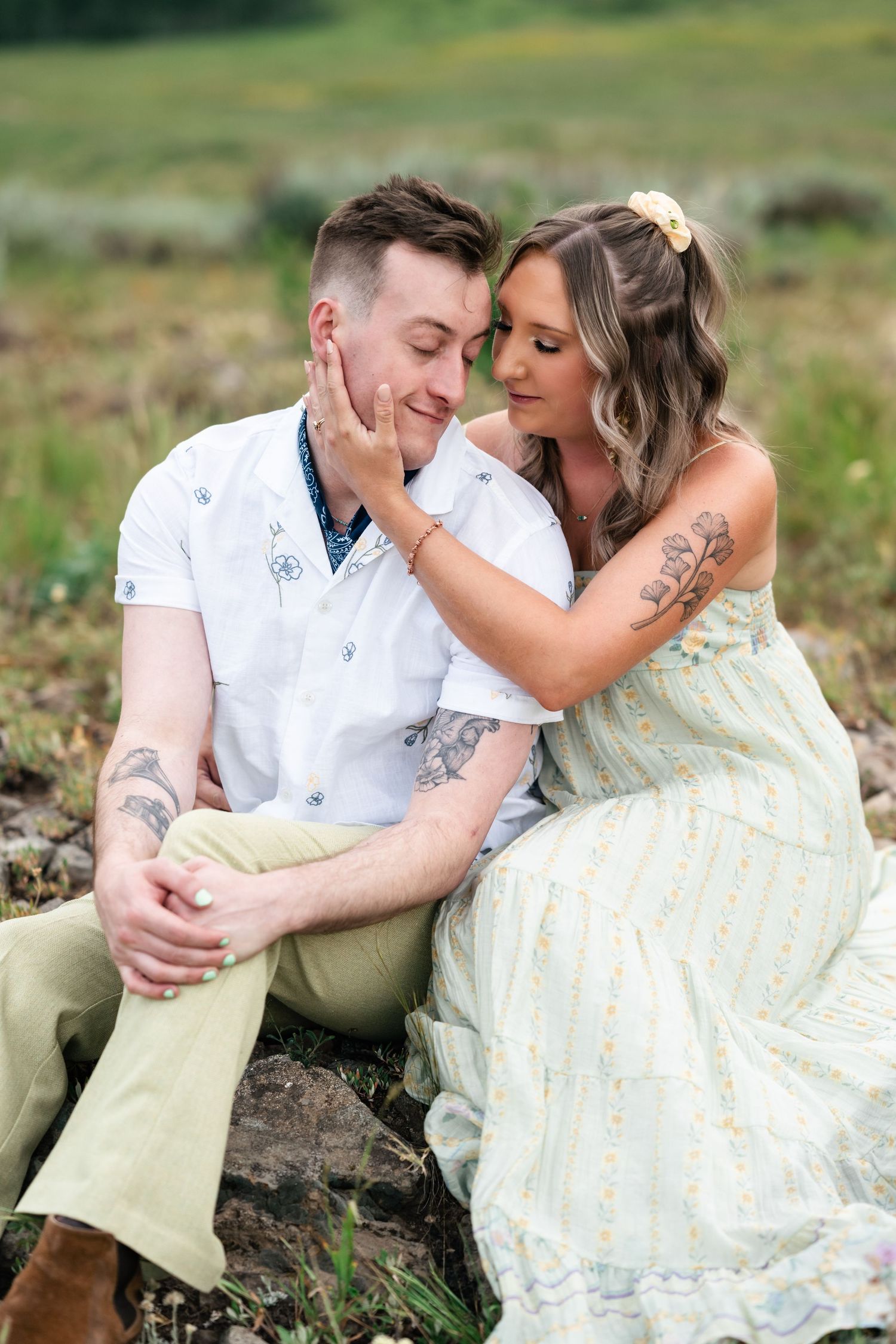 A romantic couple embraces while sitting in a grassy meadow on a sunny afternoon.