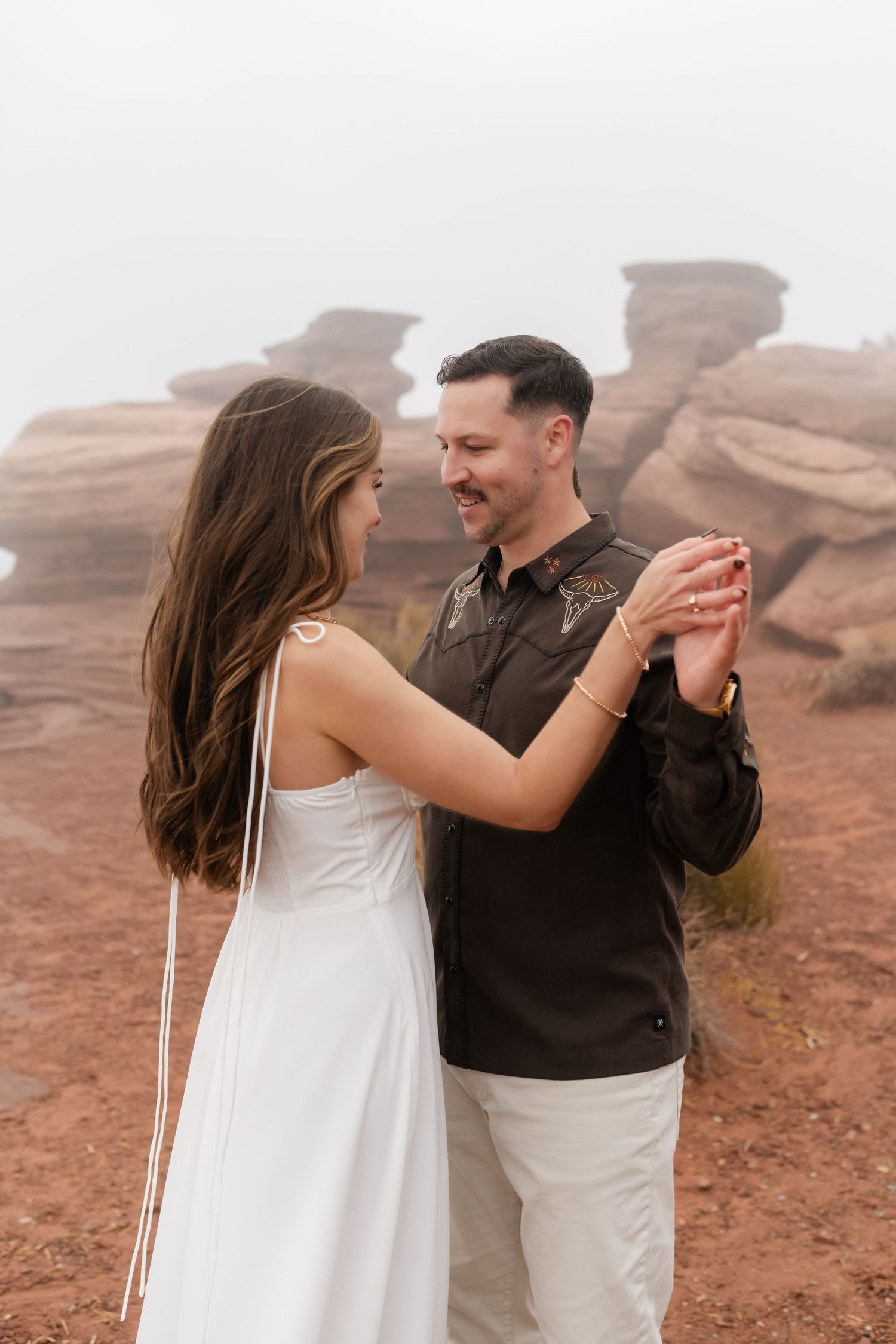 A couple dances together against a backdrop of red rock formations in a desert landscape.
