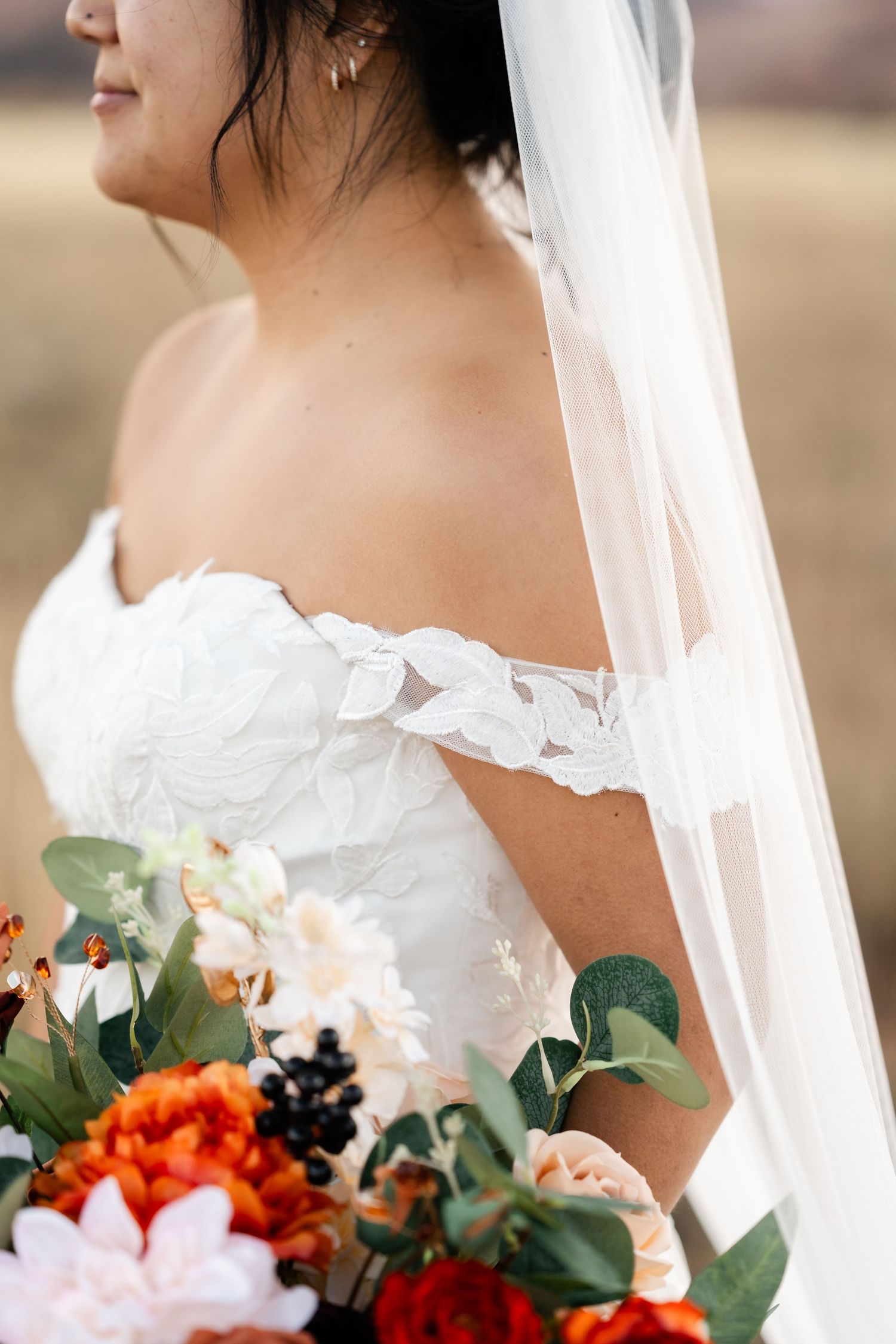 Close-up of a white bridal bouquet with orange and red flowers and green eucalyptus leaves against a blurred background.
