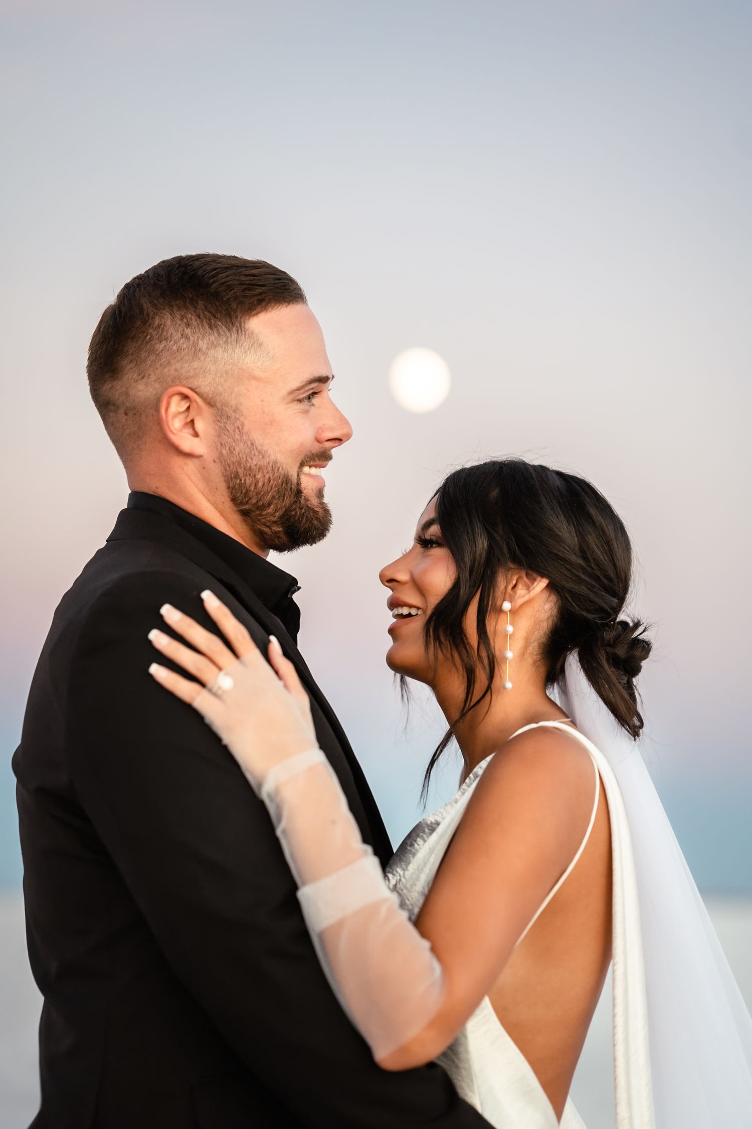 A couple shares joyful laughter during their wedding photoshoot on a bright landscape.