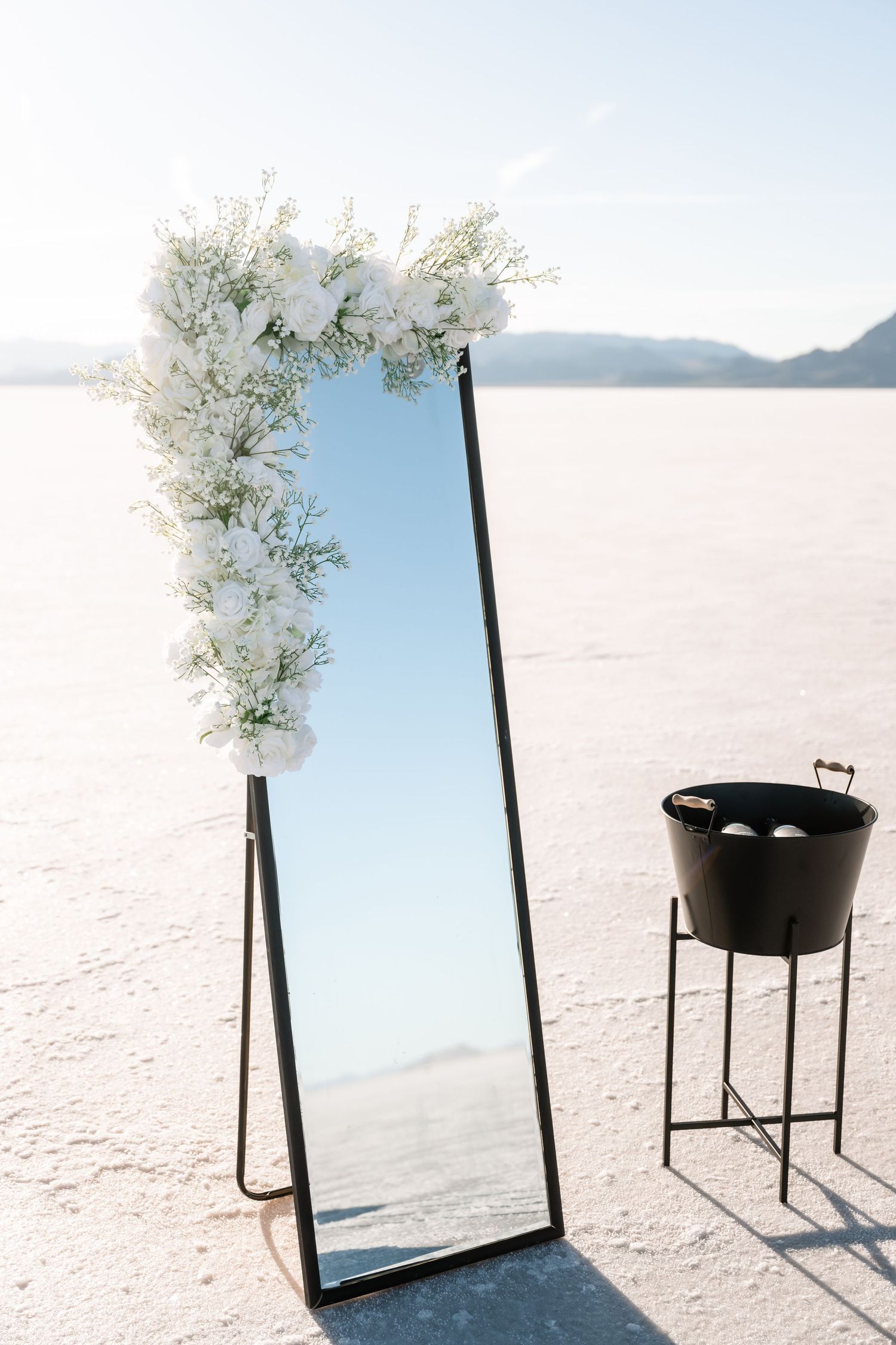 Black mirrors and floral arrangements stand against a bright white salt flat landscape.
