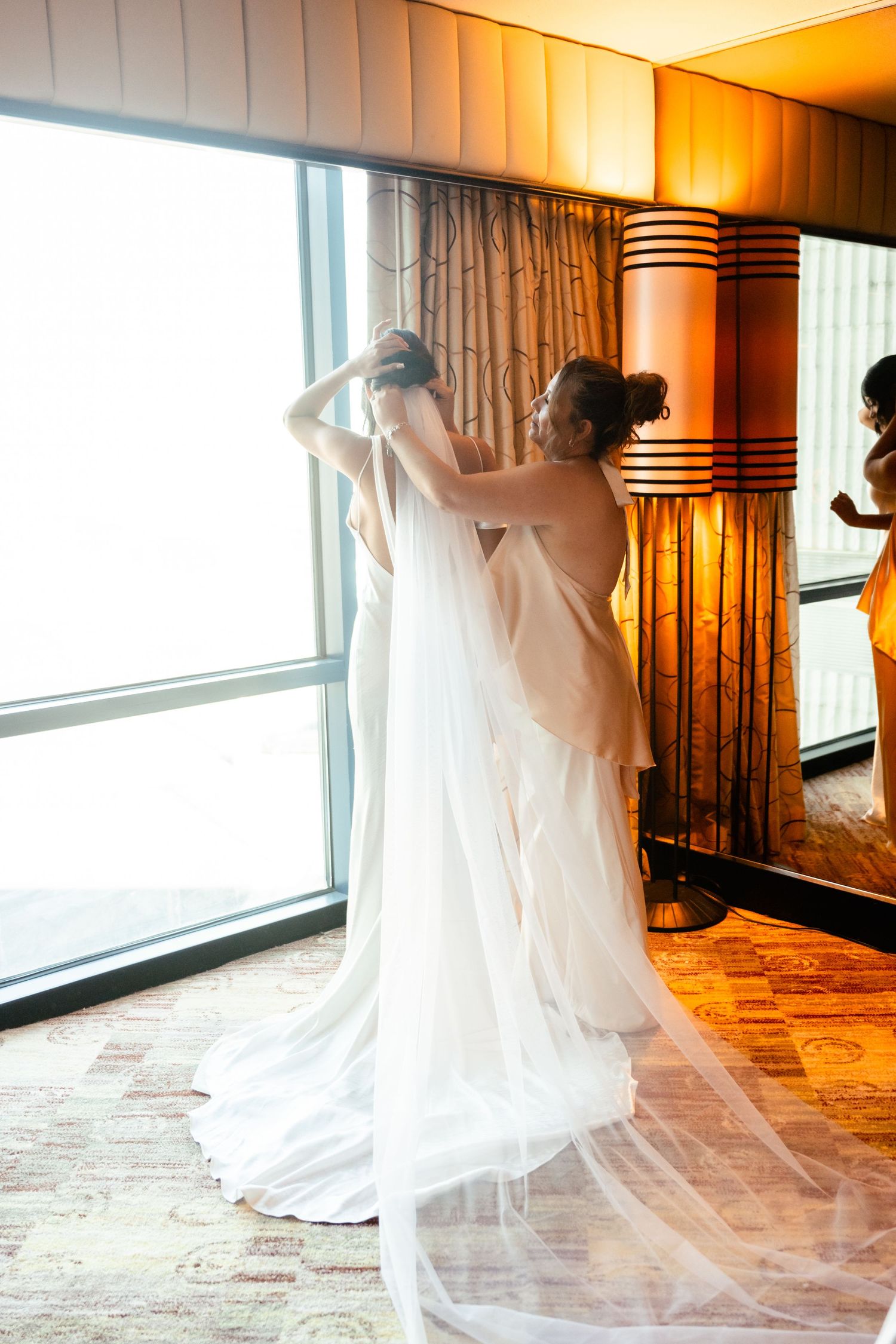 Long cathedral veil trailing behind a white wedding dress in a sunlit room.