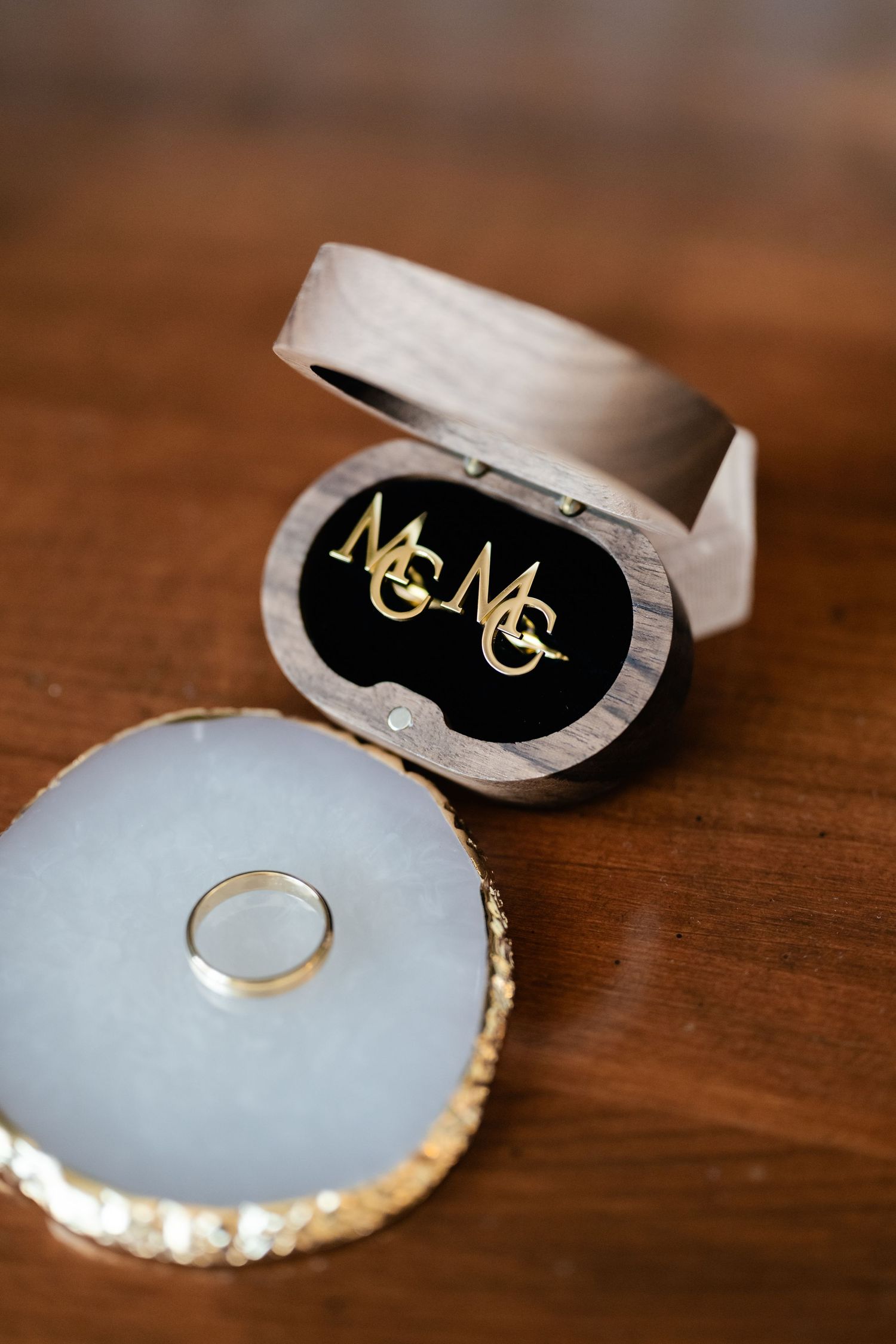 Wedding rings displayed on light blue cushions with gold monogram details on a wooden surface.