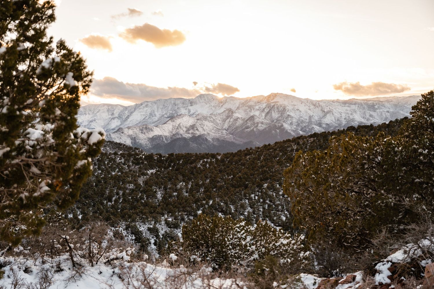 Snow-capped mountains and desert cliffs create a dramatic winter landscape at dusk.
