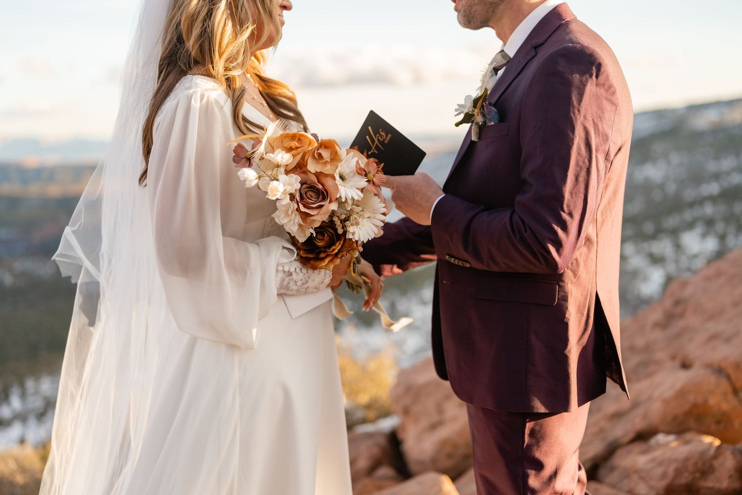 Couple in wedding attire exchanging vows against mountain backdrop.