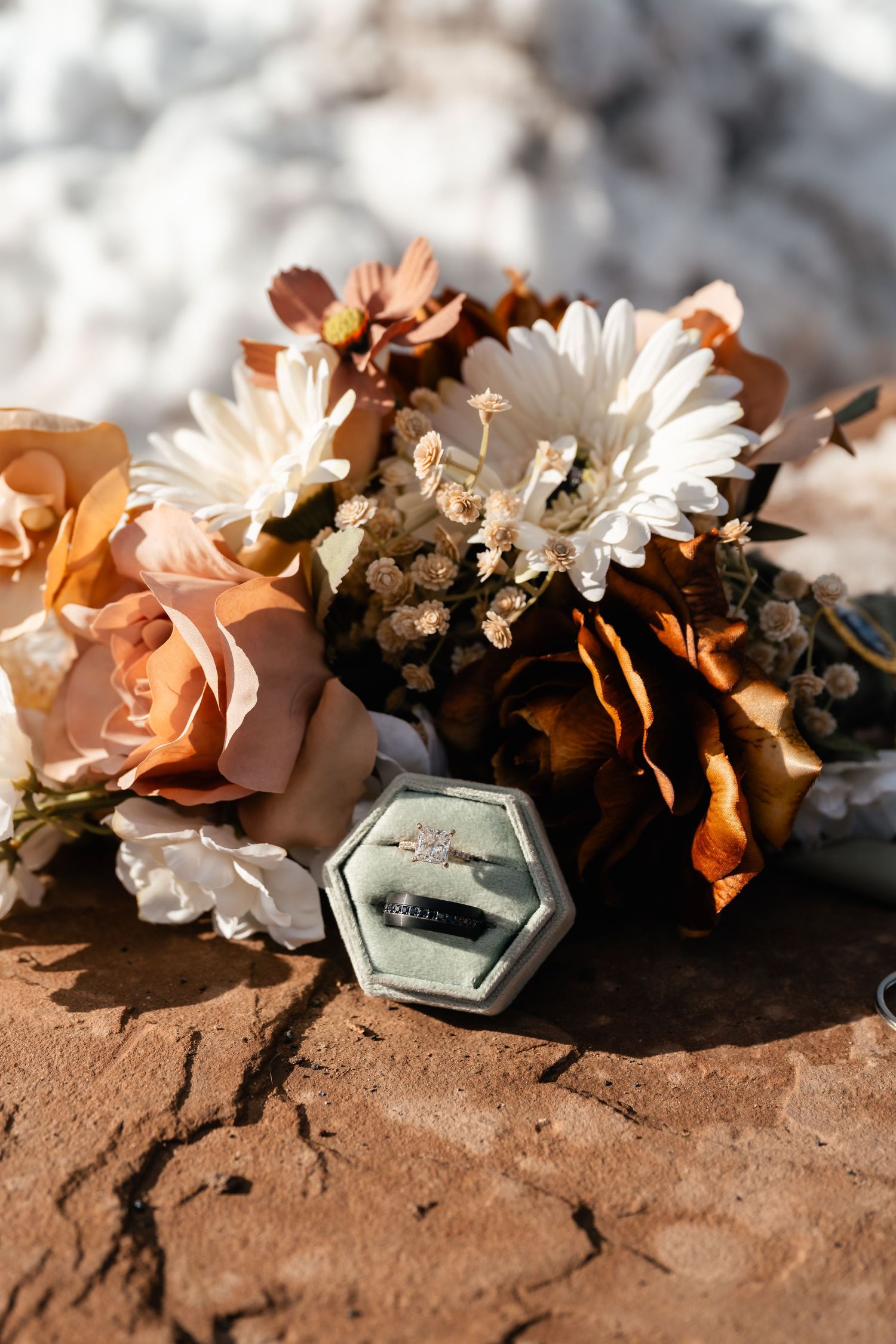 Wedding rings and delicate white flowers arranged on red desert rock.