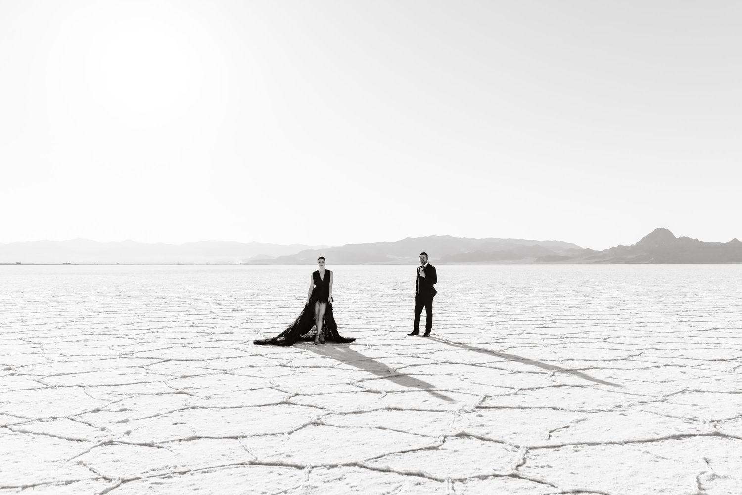 Salt Flats Photographer. Two silhouetted figures stand on a vast snowy landscape with mountains in the distance on a misty winter day.