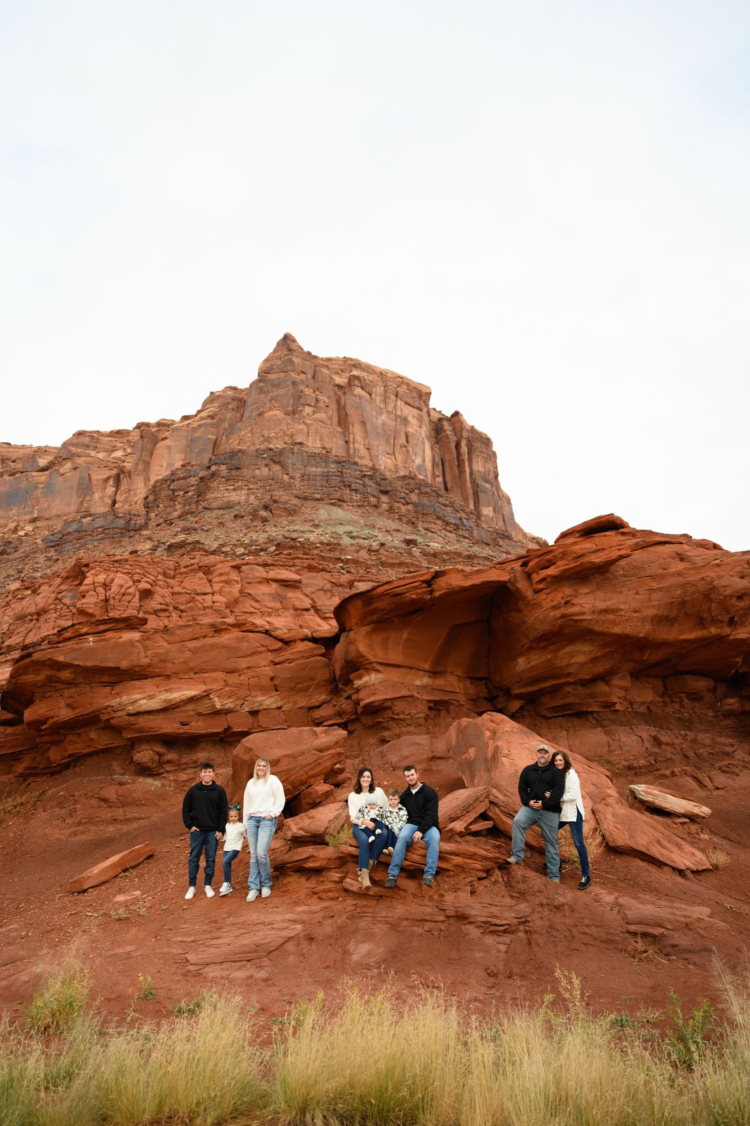 A group of people stand beneath a towering red rock arch formation in a desert setting.
