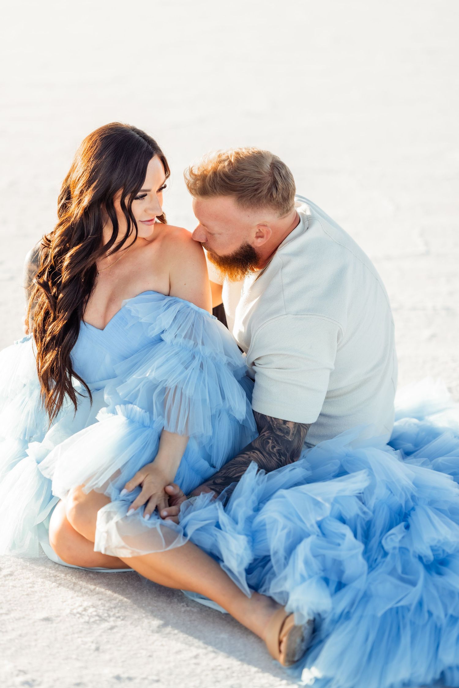 Utah Salt Flats Photographer. Romantic couple in blue dress and casual wear embrace on white salt flats during photo session.