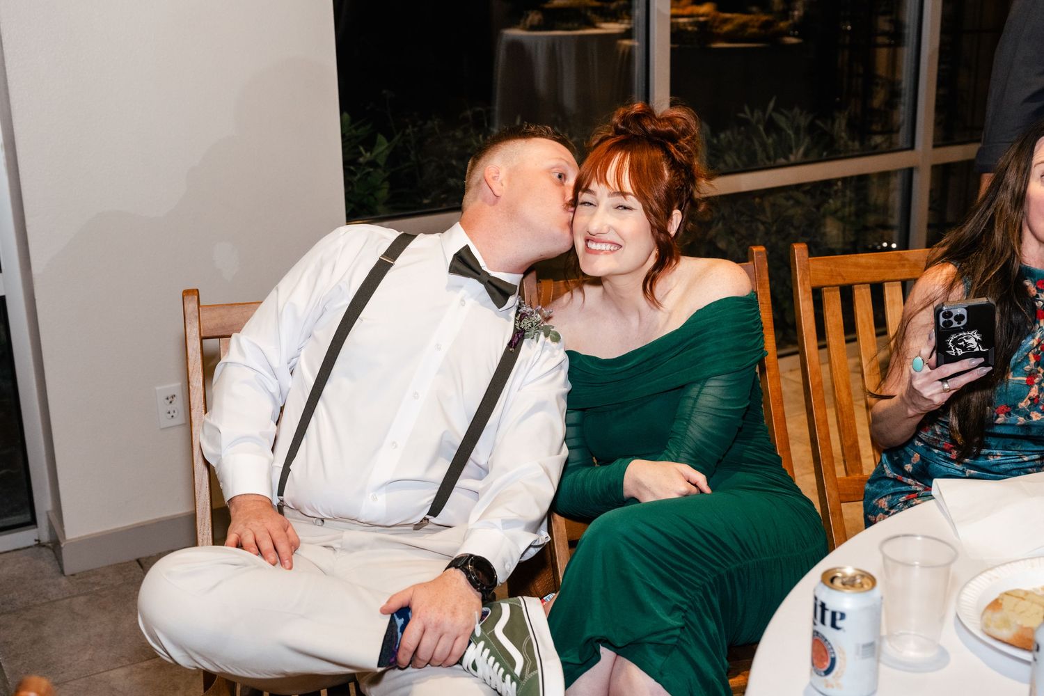 A couple shares an affectionate moment at a dinner table, with the woman wearing an elegant emerald green dress.