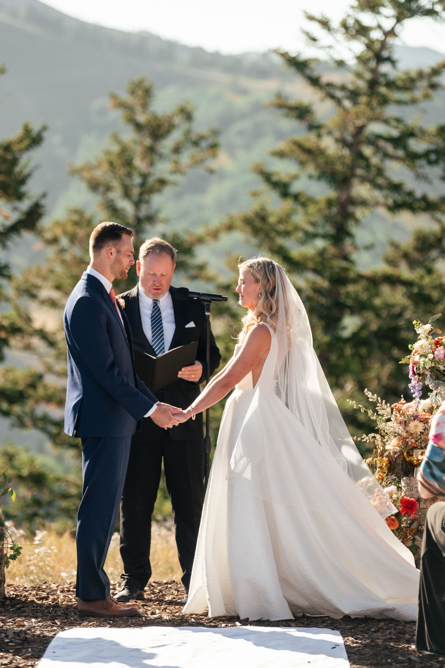 Mountain wedding ceremony takes place on scenic overlook with evergreen trees and white aisle runner. Park City Wedding Photographer.