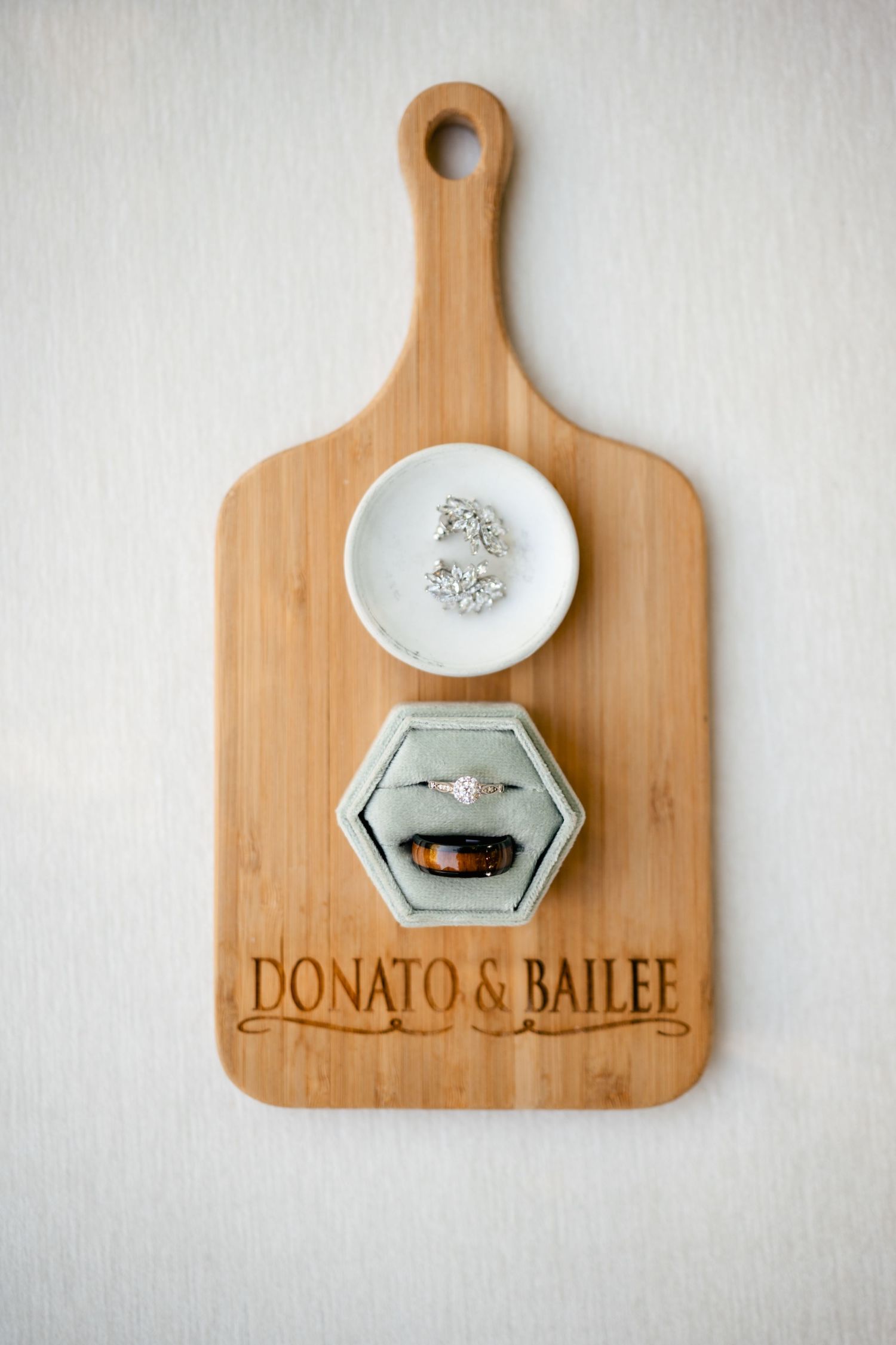 Wedding rings displayed on a personalized wooden cutting board with 'DONATO & BAILEE' engraved on it.