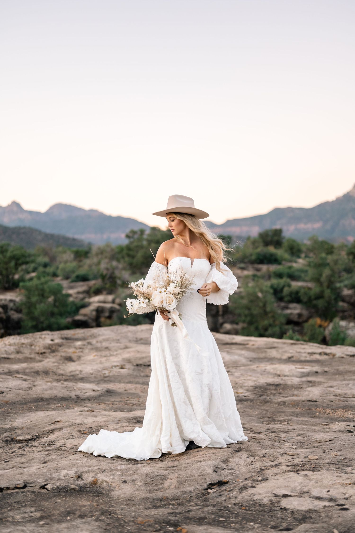 Bridal photo showing full length white gown and western hat in mountain setting.