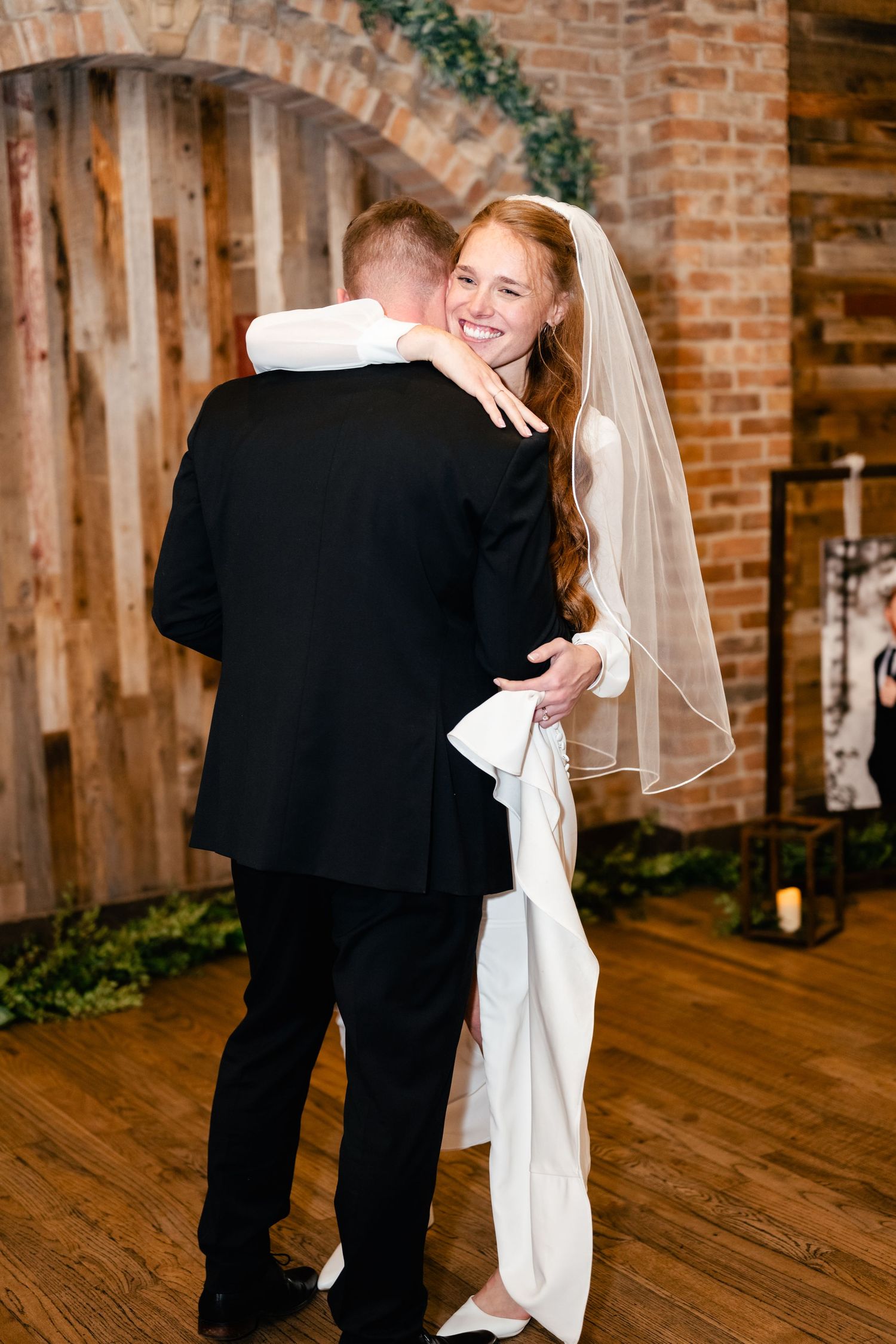 A joyful wedding moment captured at an indoor brick-walled venue with elegant decor and hardwood flooring.