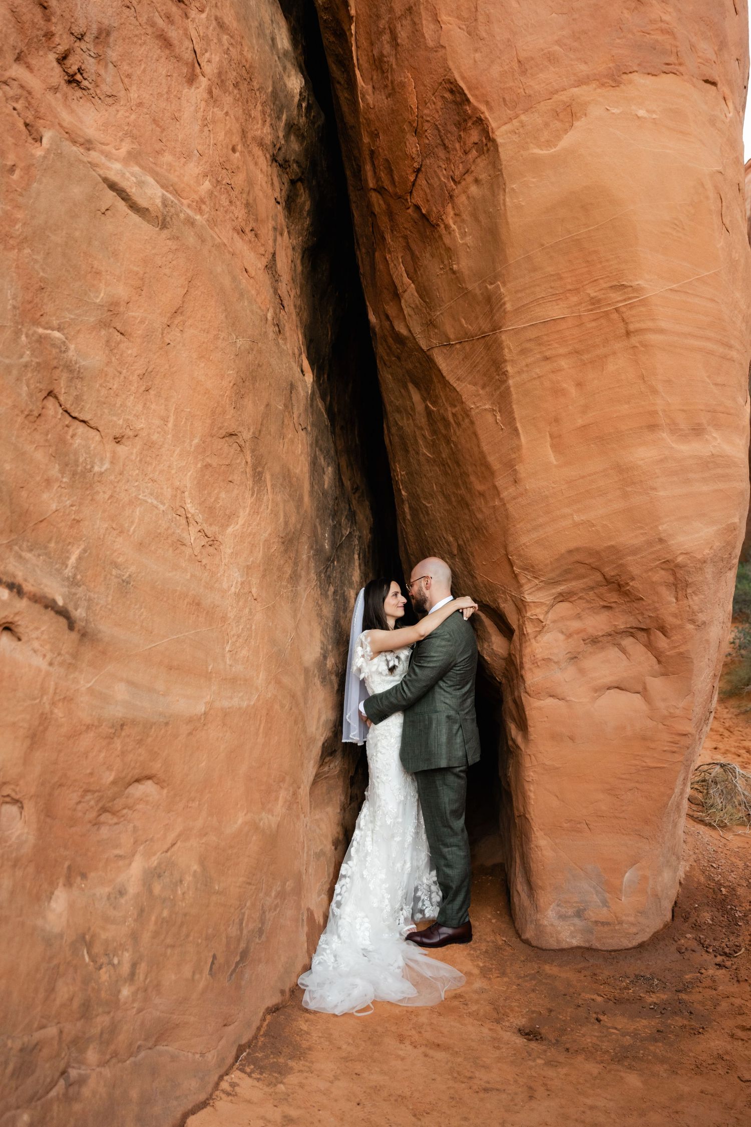A wedding couple shares an intimate moment between towering red sandstone walls.