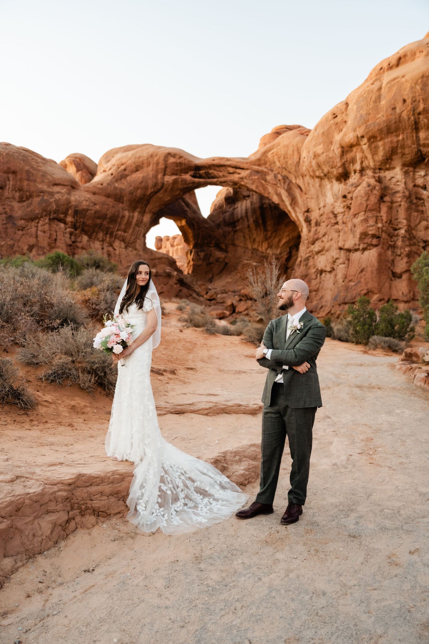 Wedding portraits in front of natural stone arches with desert landscape backdrop.