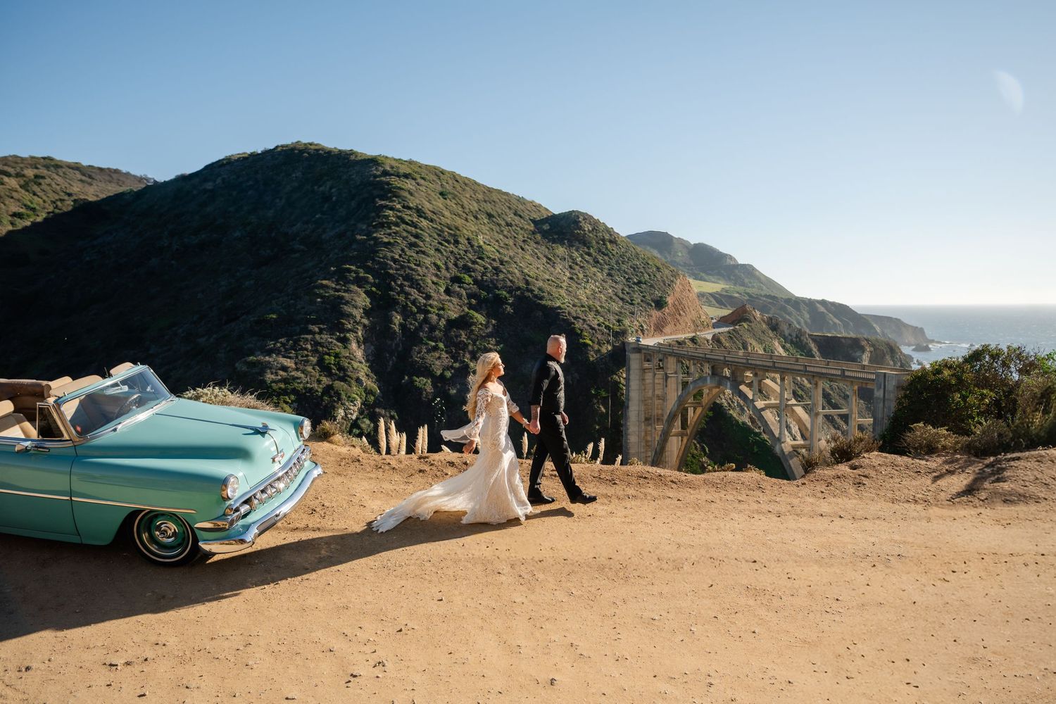 Scenic mountain coastline view with classic car silhouetted against blue sky.