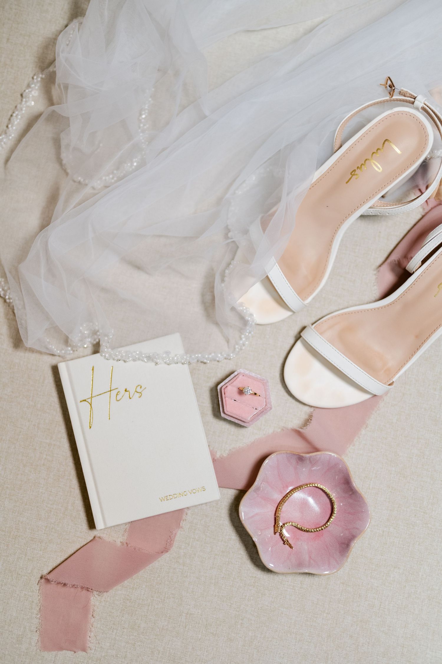 White bridal shoes and wedding stationery arranged with pink floral accents on a light background.