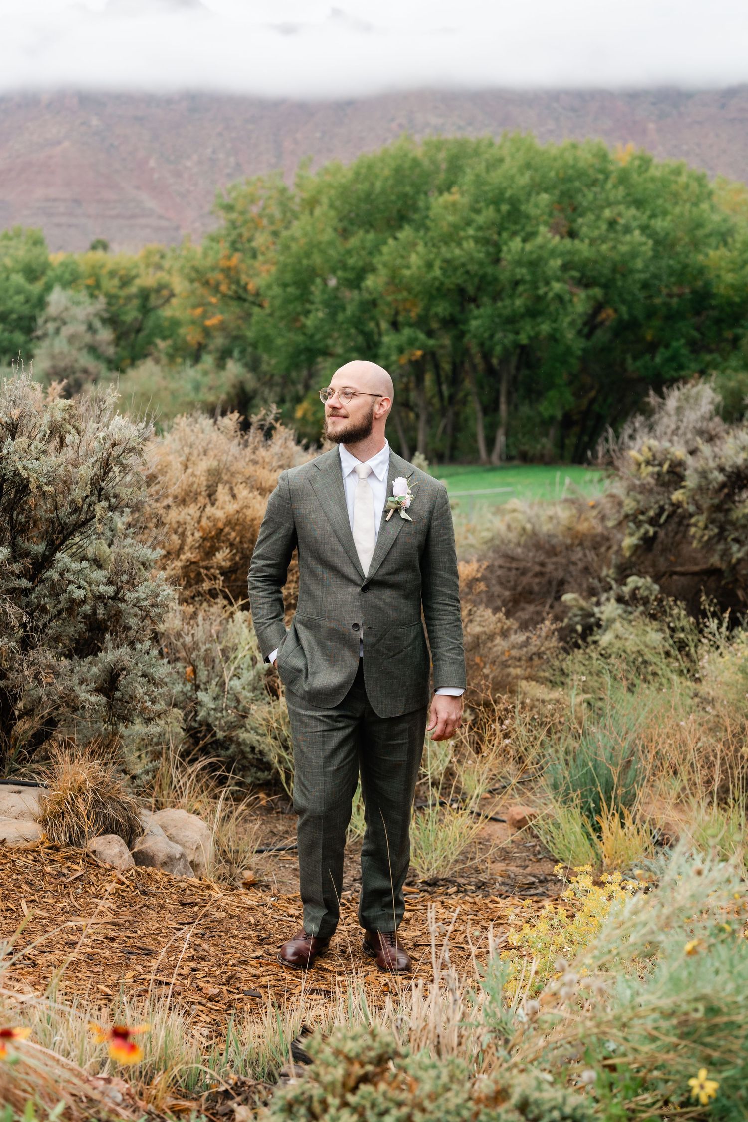 Wedding party members stand among desert brush and wildflowers in formal attire.